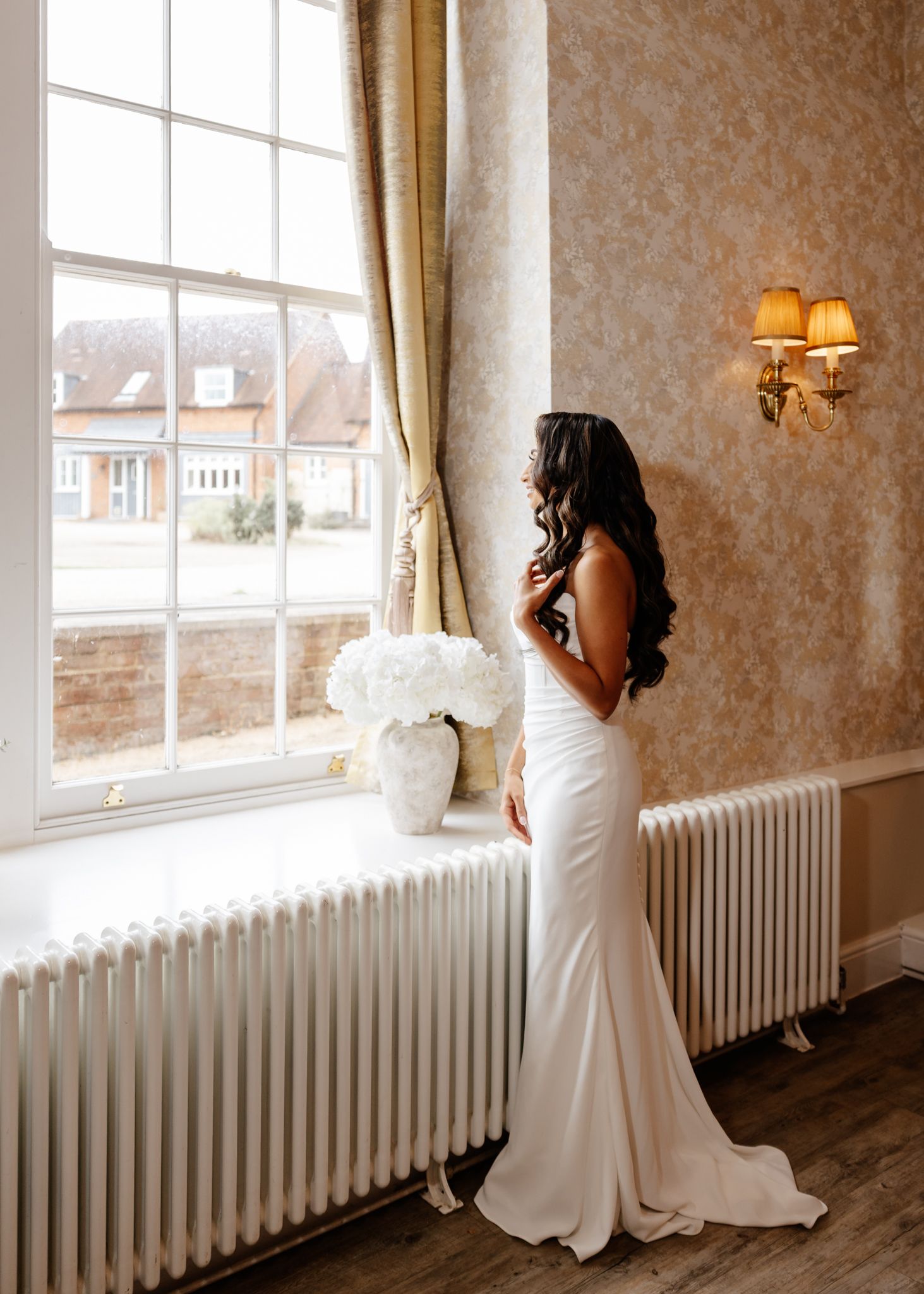 A panoramic view of a bridal gown against a vintage interior with white radiators and large windows.