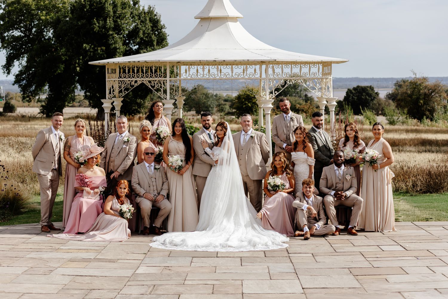 Wedding party in neutral colors poses together on stone patio with scenic mountain views in background.