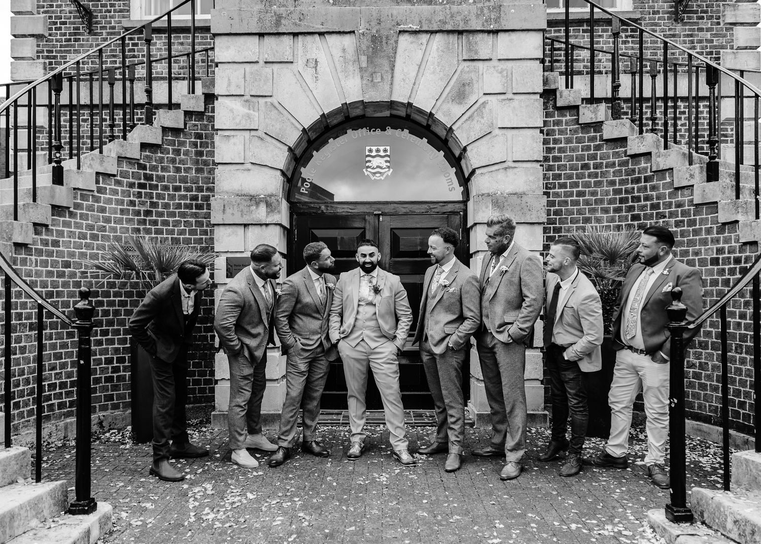 Black and white panoramic photo of wedding party members seated on brick steps in formal attire.