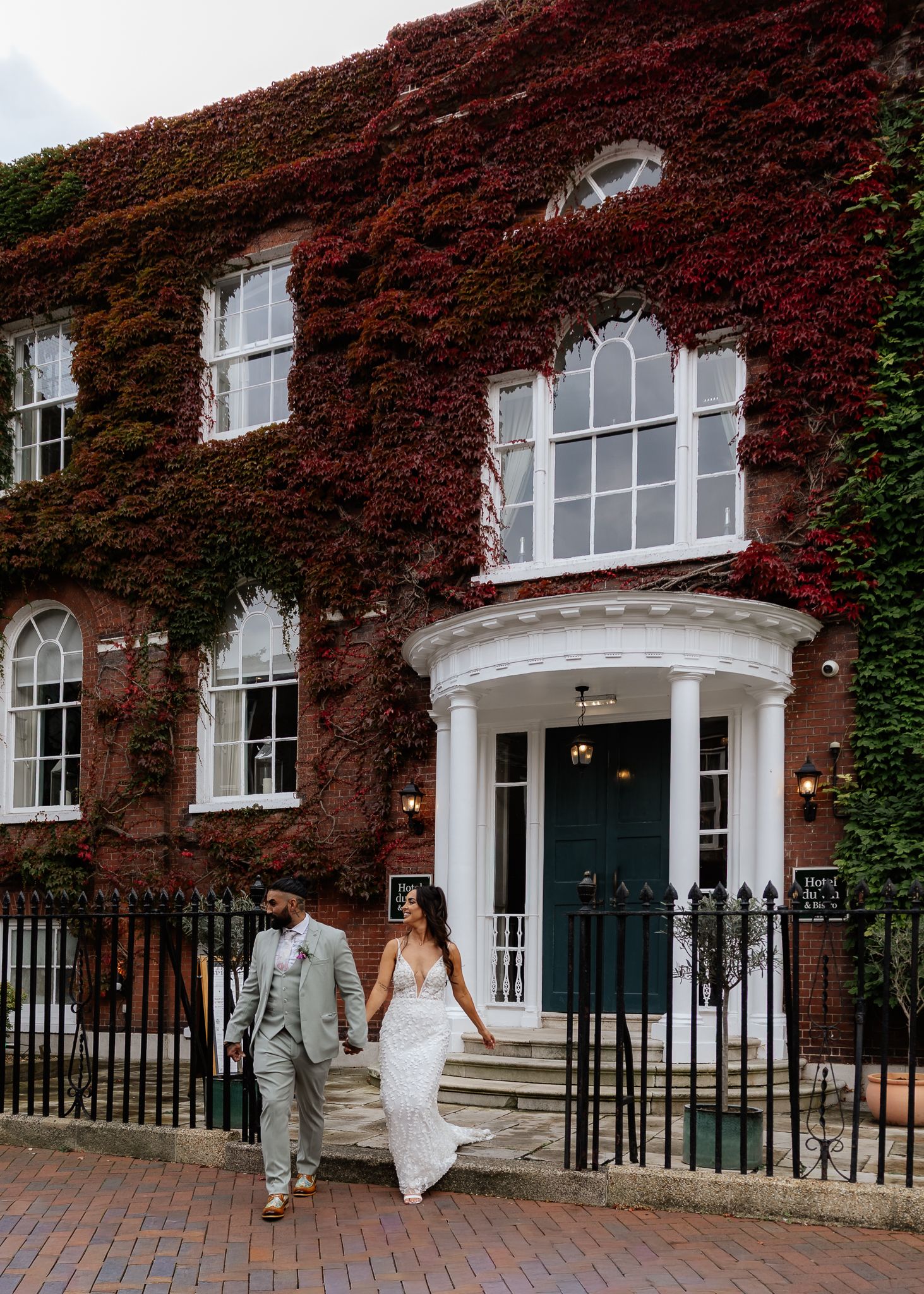 Elegant couple walks together in front of historic brick building covered in vibrant red autumn ivy.