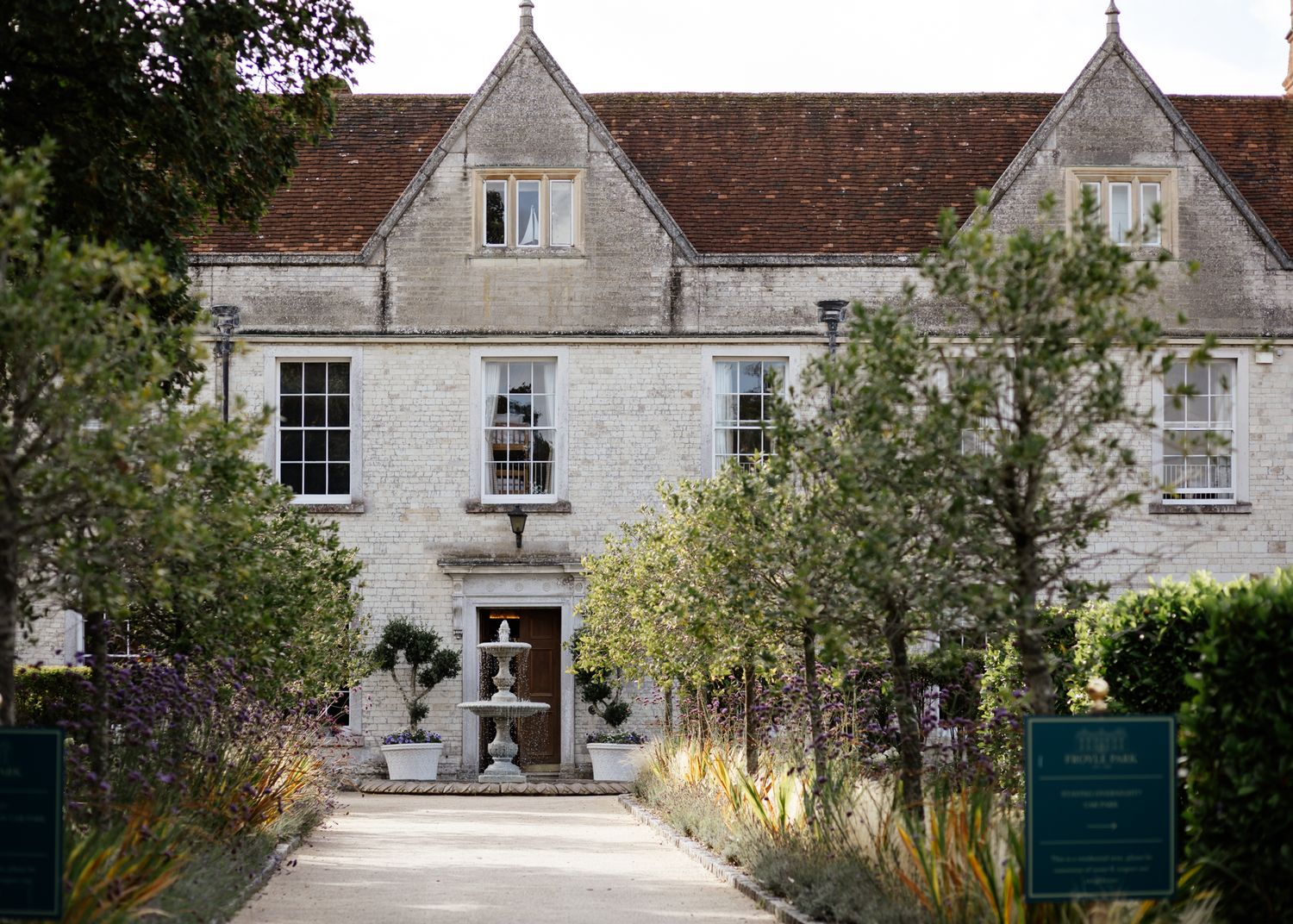 A series of stone buildings with ornate architectural details and gabled roofs form a historic estate entrance.