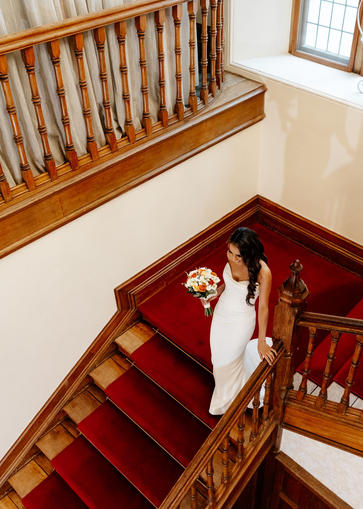 A sequence of photos showing someone in a white wedding dress descending elegant wooden stairs with red carpeting.