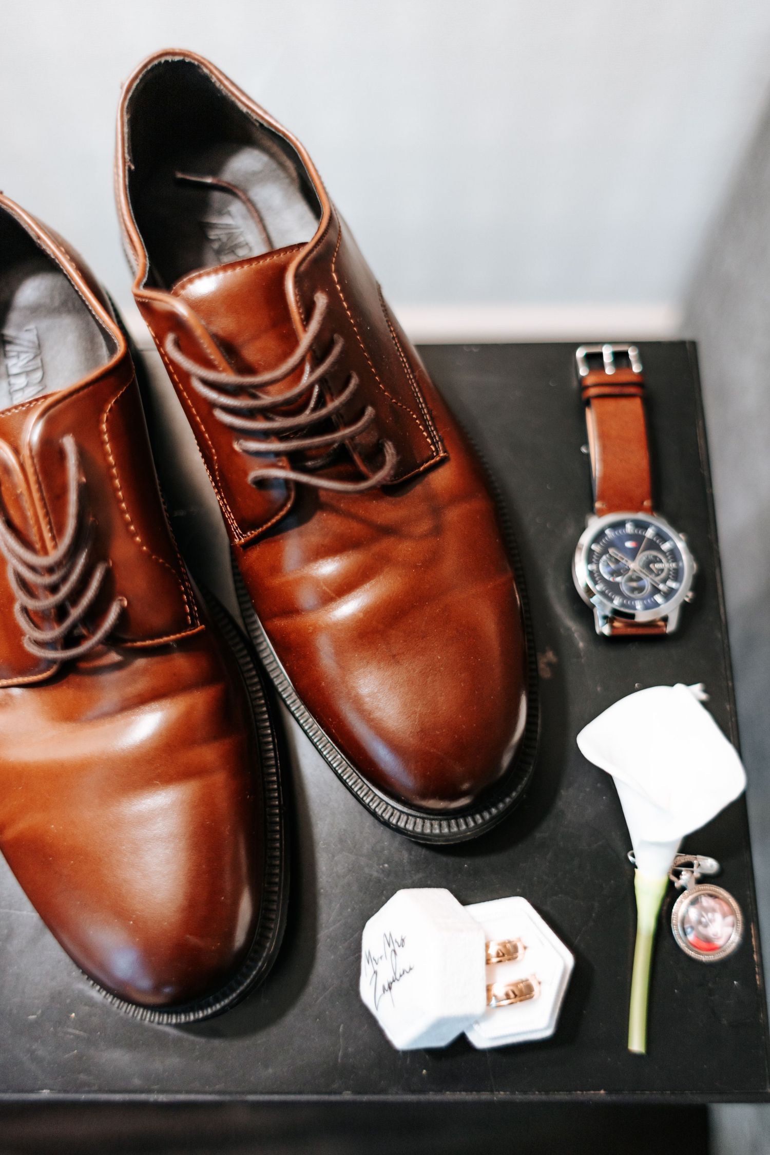 Brown leather dress shoes, watch, cufflinks, and boutonniere arranged as groom wedding day accessories.