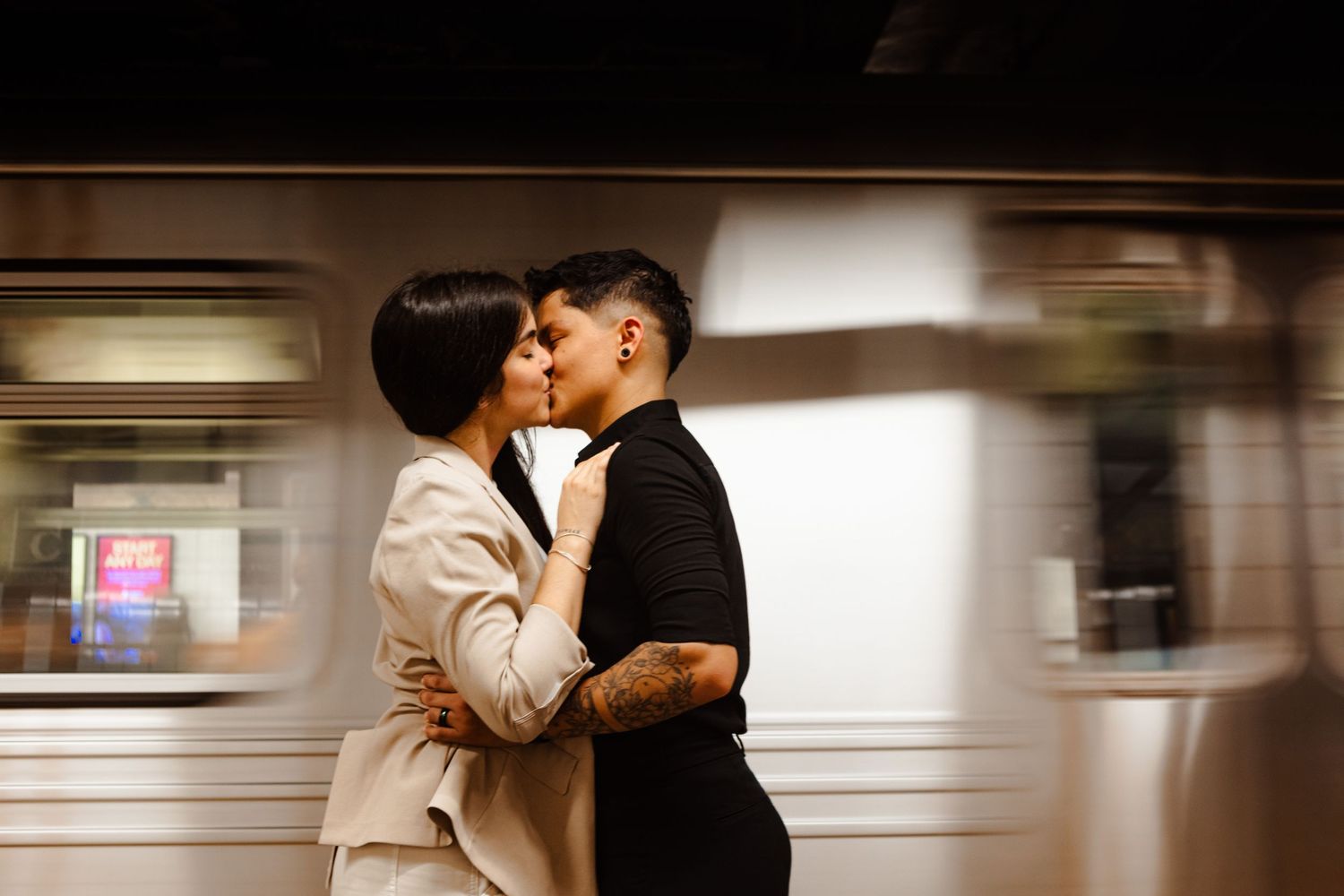 Couple sharing a kiss on a subway platform with a blurred train passing behind them.