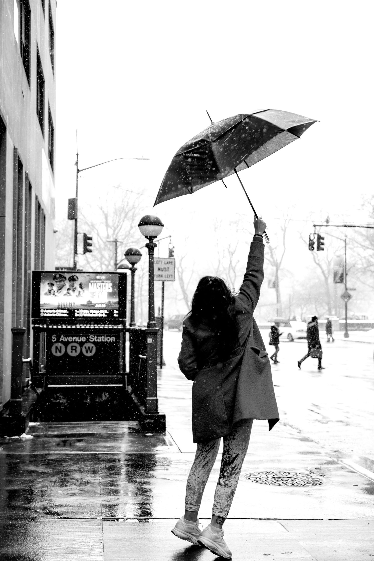 Black and white photo of woman raising umbrella in NYC snowstorm near subway.