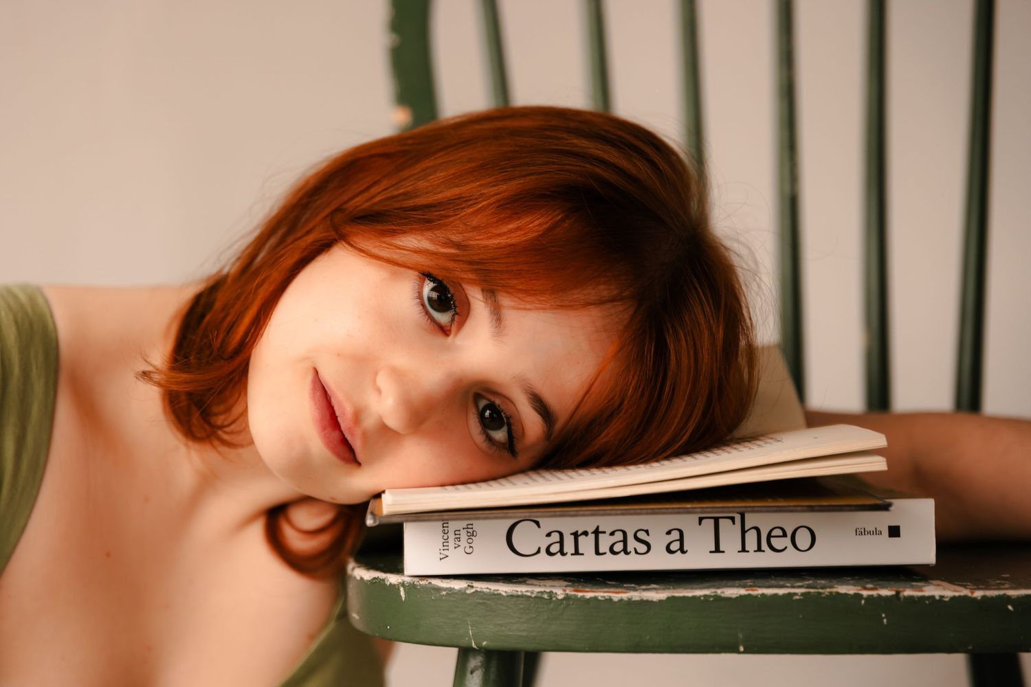 Young redhead woman resting her head on books including Cartas a Theo on a chair.
