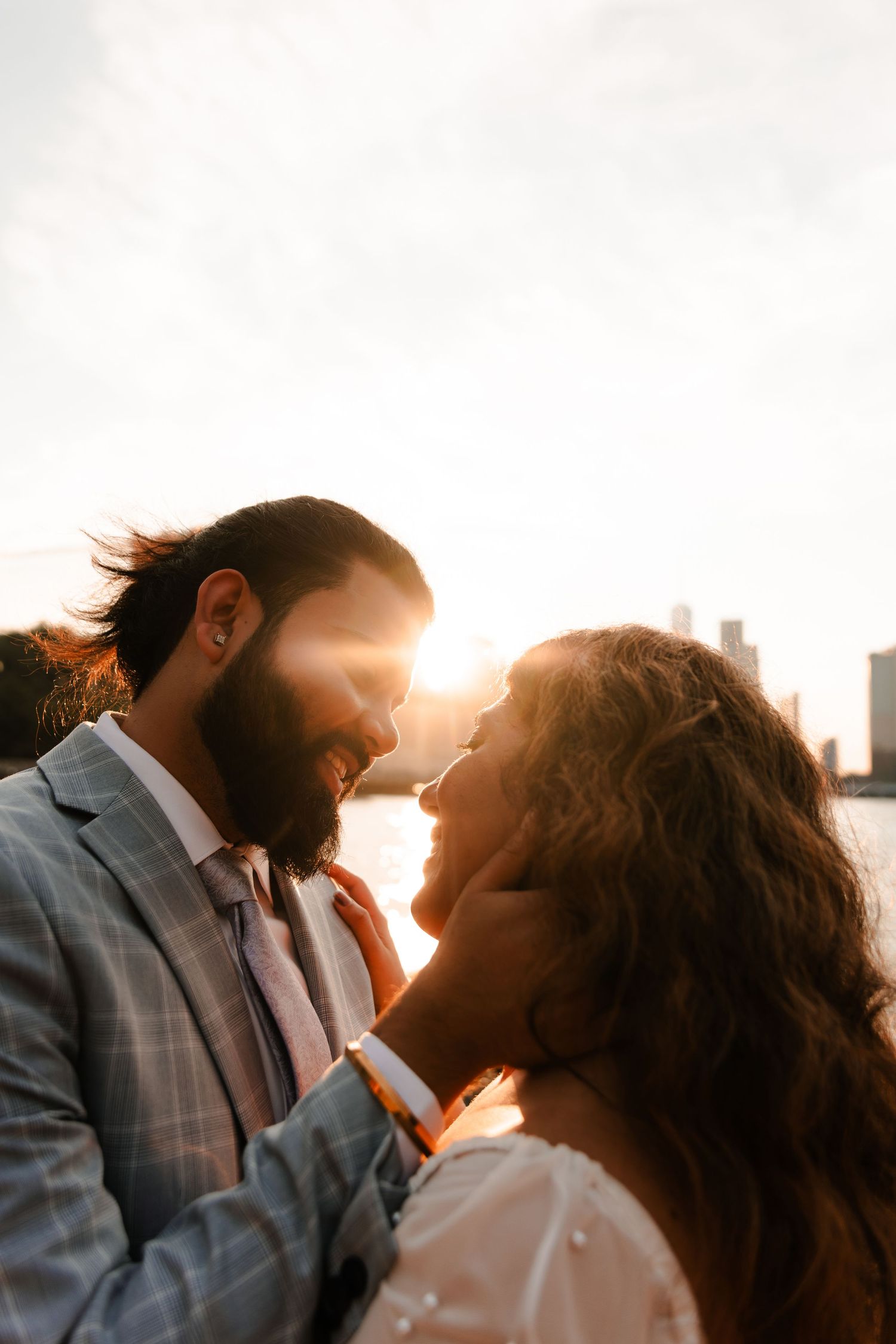 Couple shares a romantic moment at golden hour with city skyline glowing behind them at sunset.