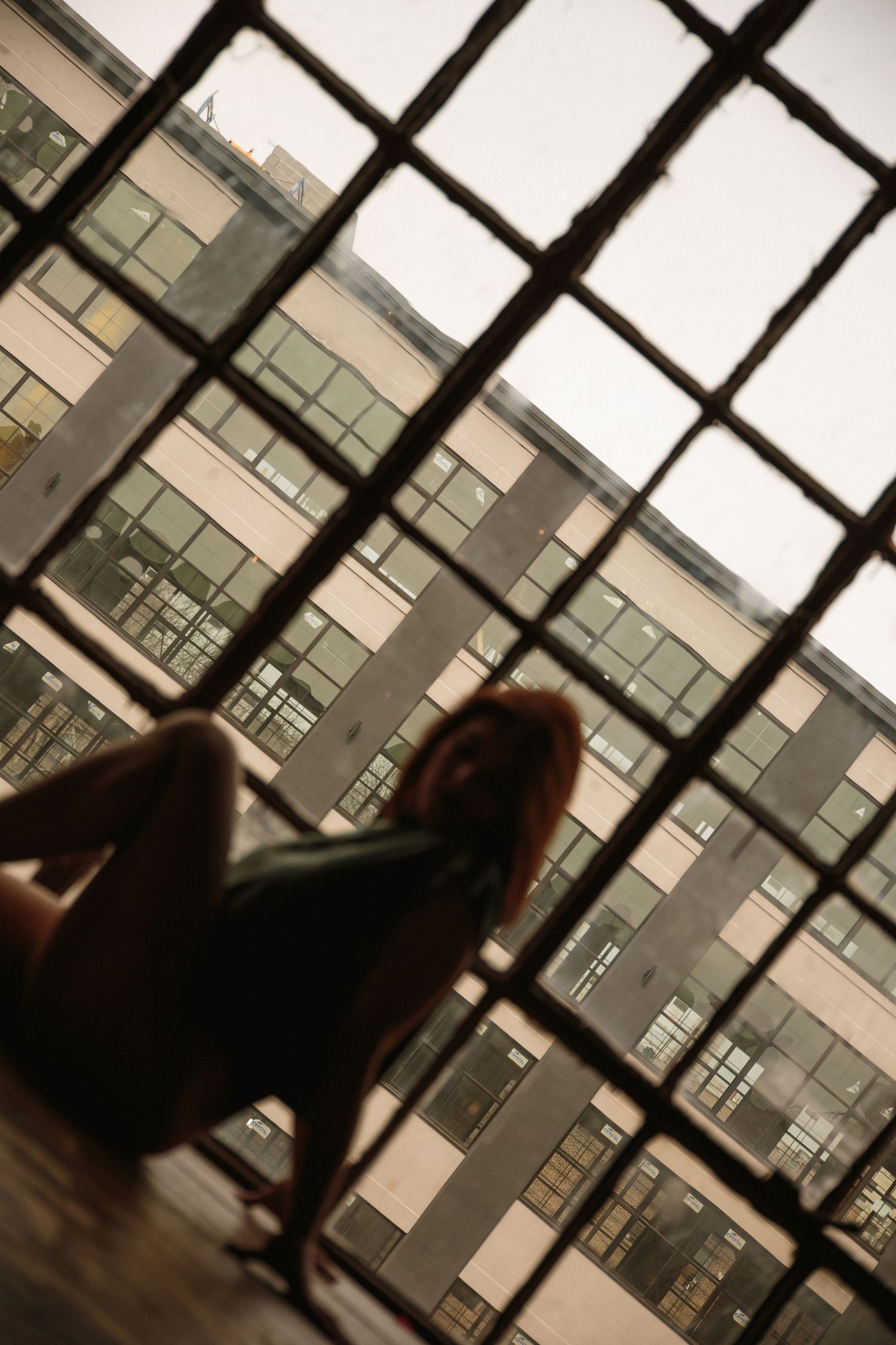 Silhouette of a person viewed through a grid window overlooking a modern building exterior.