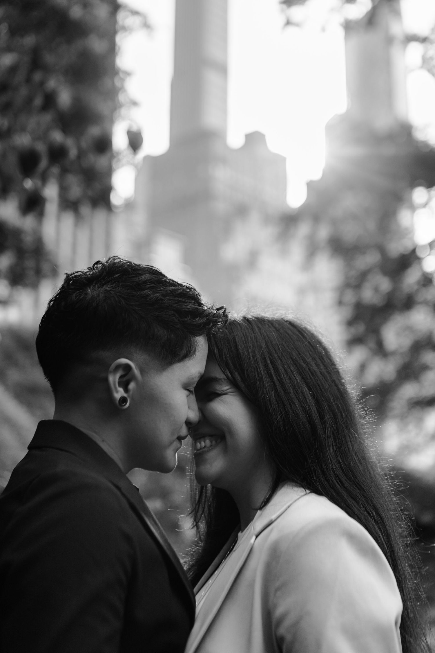 Black and white photo of couple smiling and touching foreheads in romantic outdoor setting.