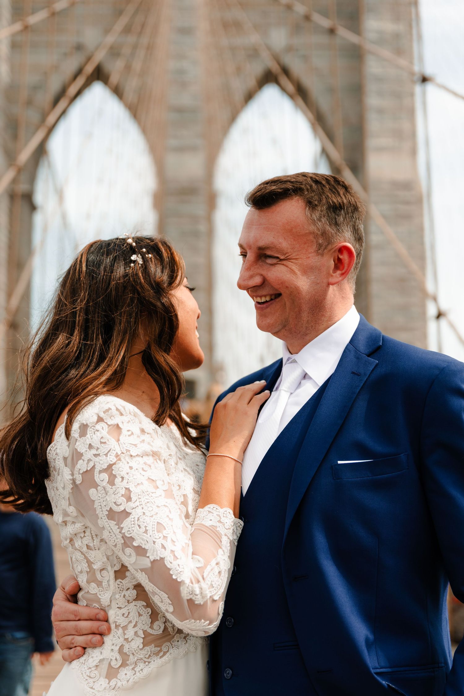 Bride adjusting groom's tie while smiling at each other on the iconic Brooklyn Bridge.