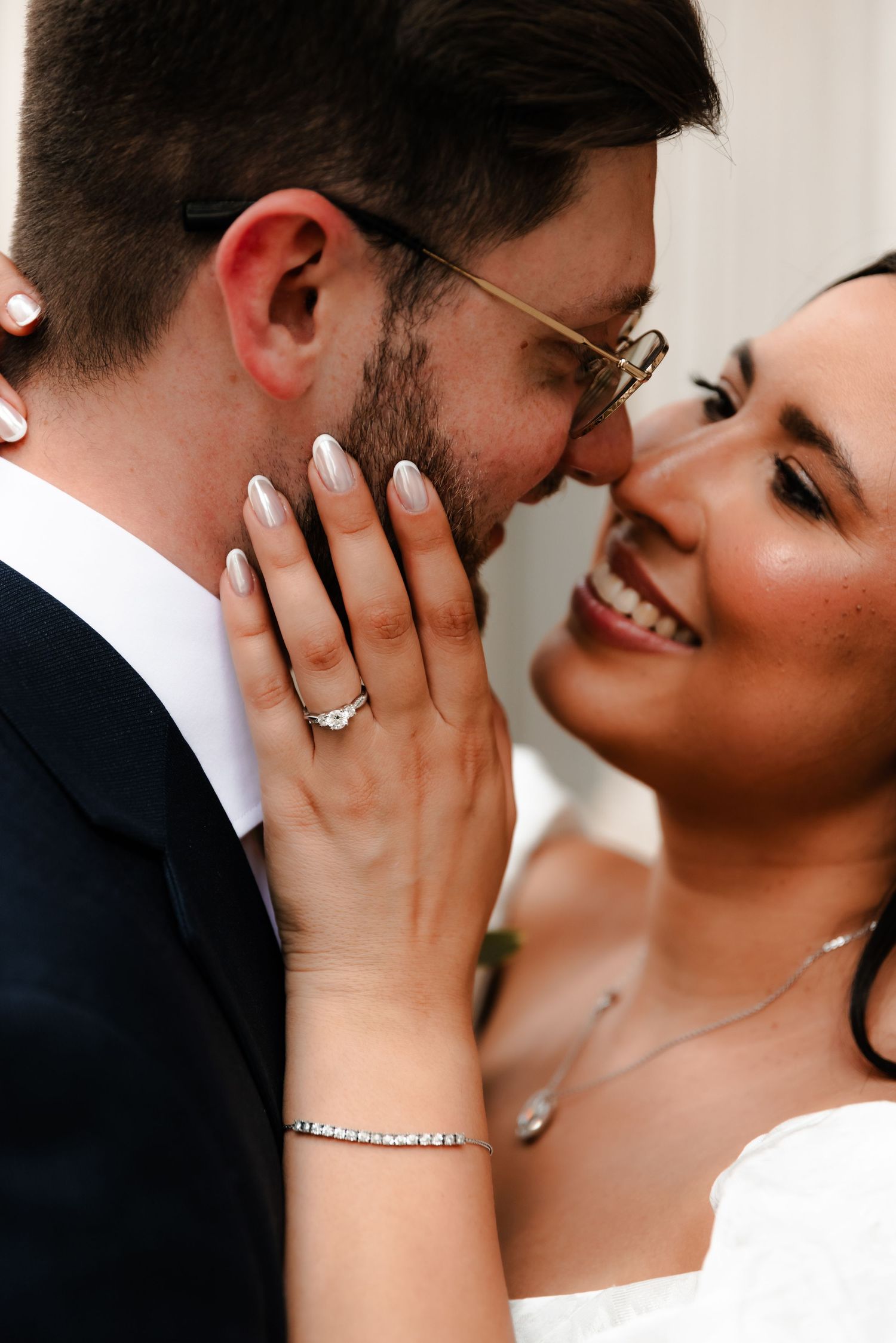 Close-up of smiling bride touching groom's face, showcasing diamond engagement ring and bracelet.