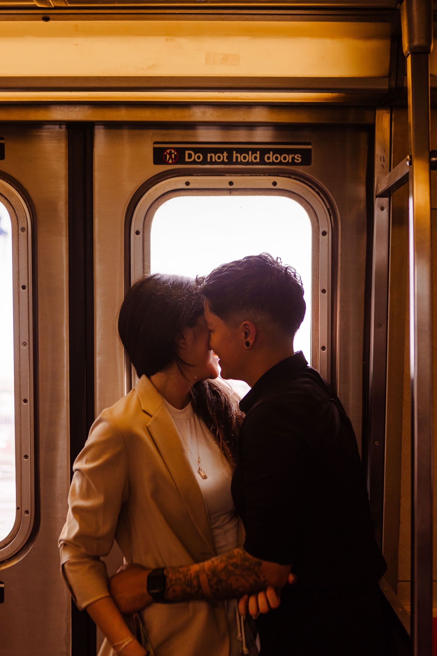 Couple about to kiss standing by subway train doors with Do Not Hold Doors sign above.
