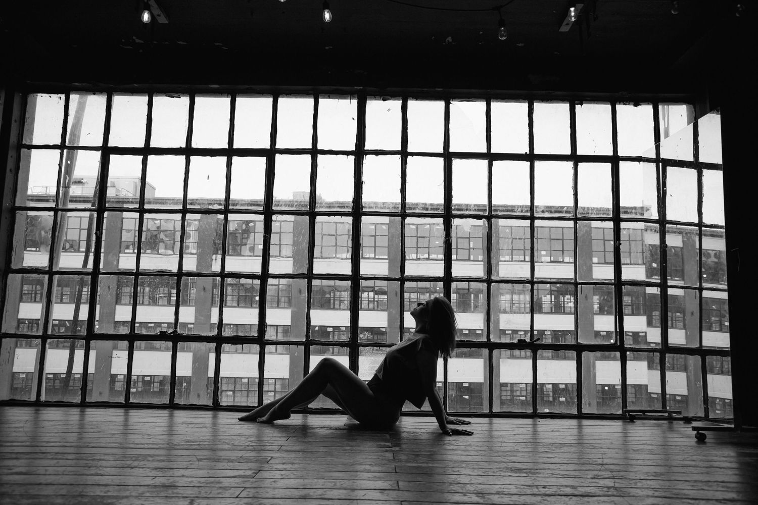 Black and white silhouette of a woman sitting on a studio floor against large windows.