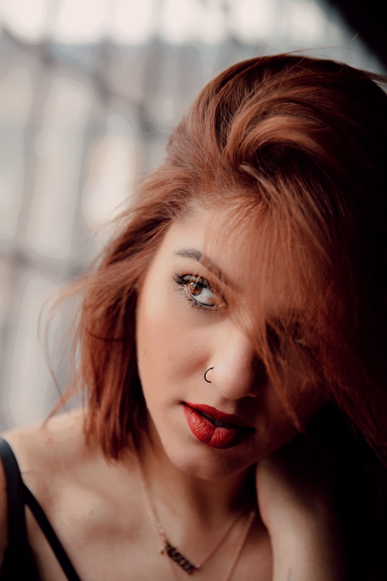 Close-up portrait of a redhead woman with red lips, nose ring, and expressive eyes.
