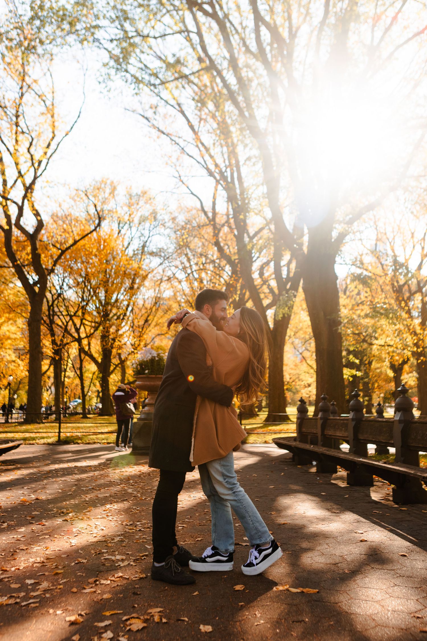 Couple kissing in Central Park during golden autumn sunset surrounded by fall foliage.