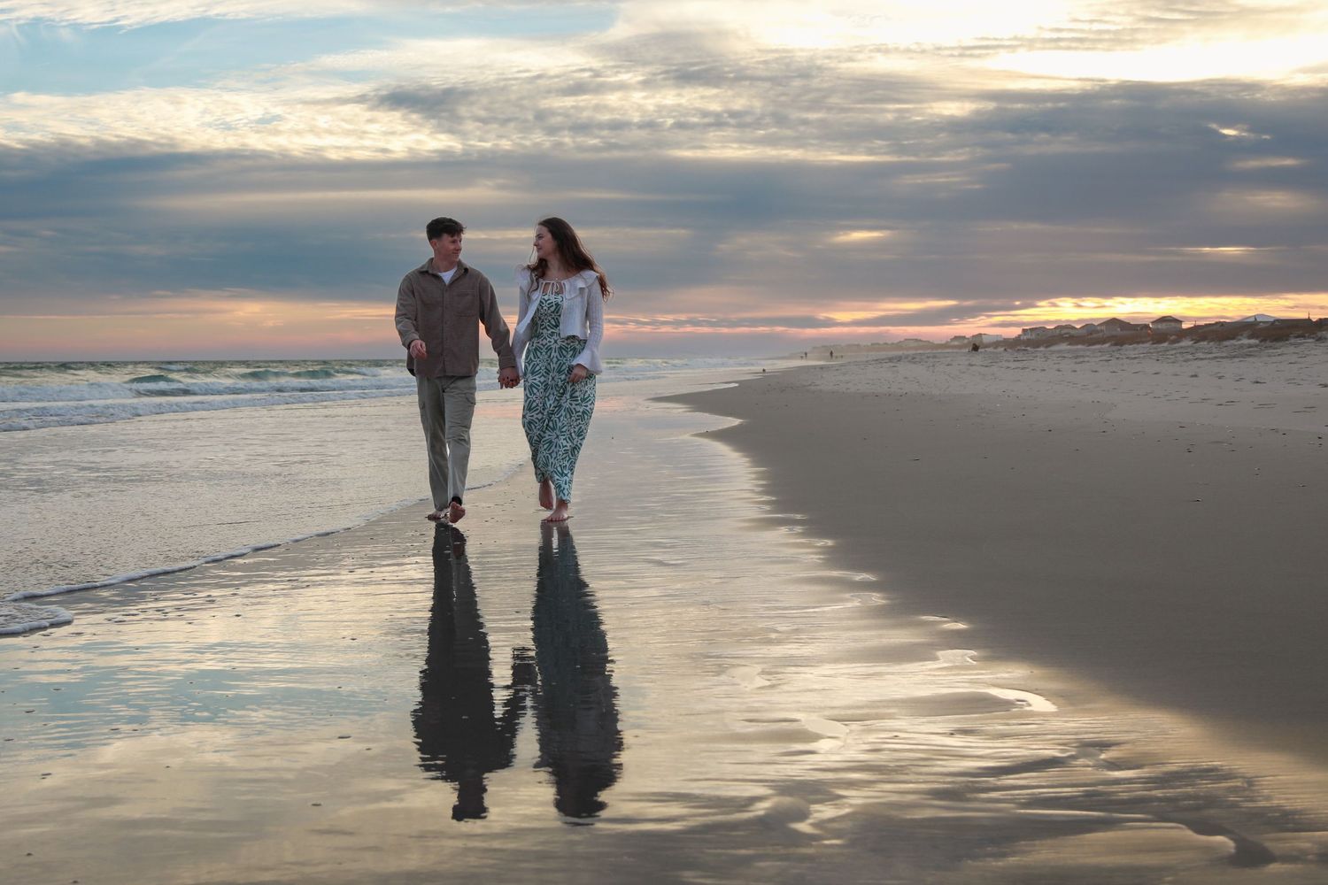 Couple walking hand in hand on a sandy beach at sunset with reflections on wet sand.