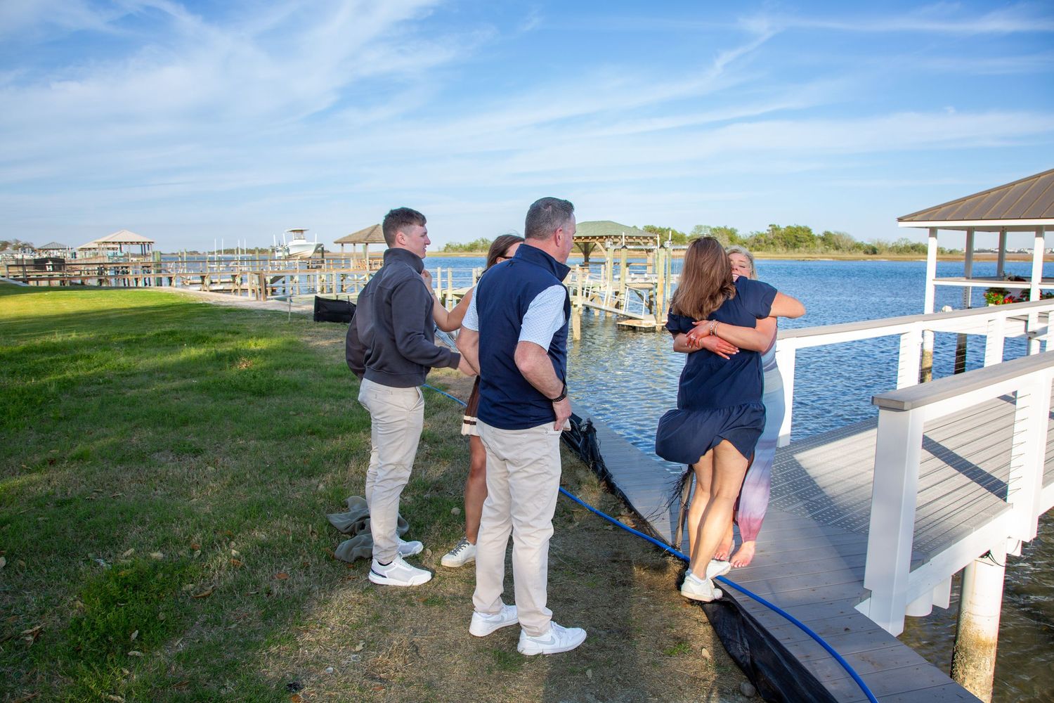 Group of friends socializing on a waterfront dock near a marina on a sunny day.