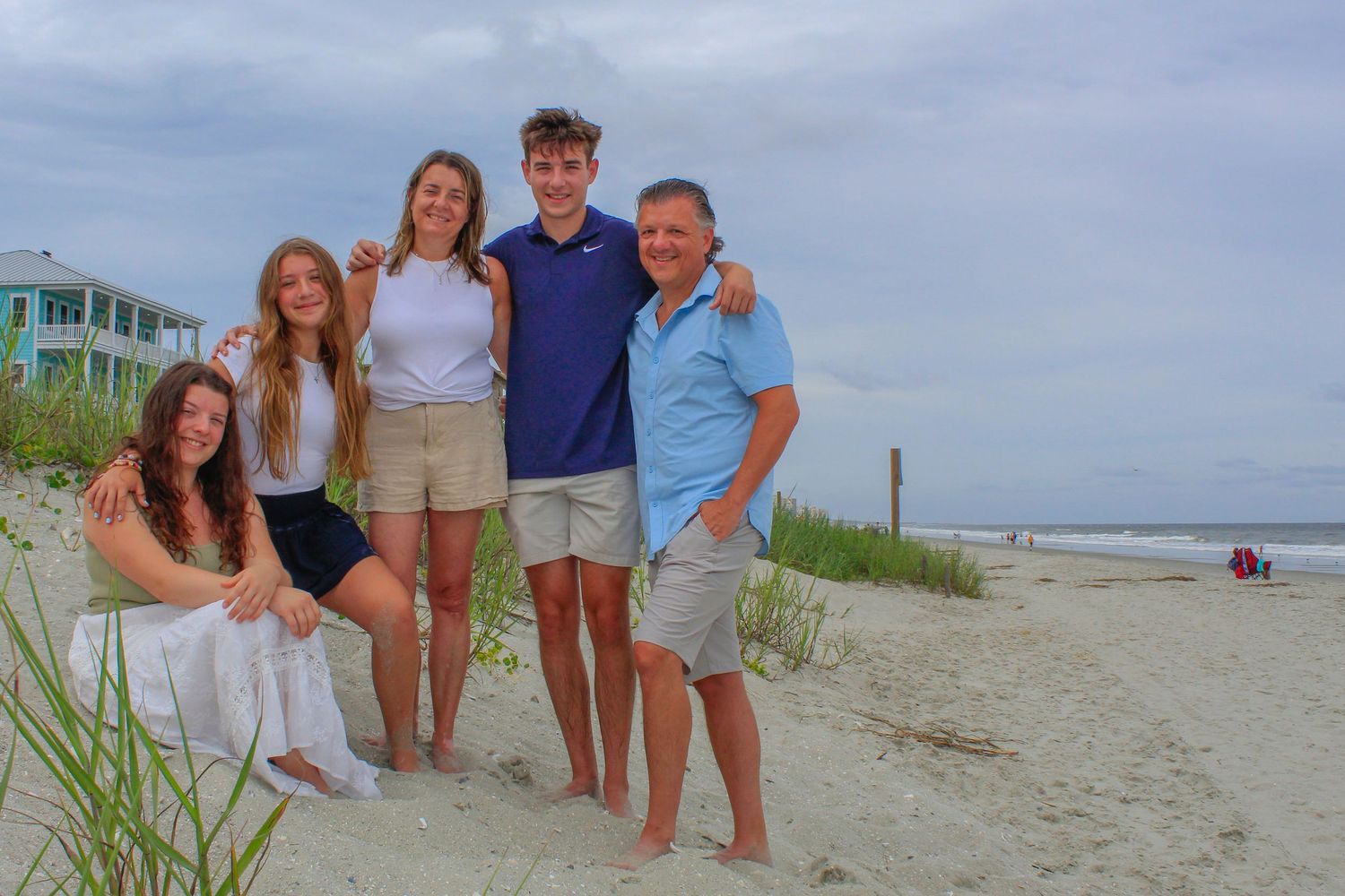 Group of people enjoying a sunny day at the beach with sand dunes and ocean waves in the background.