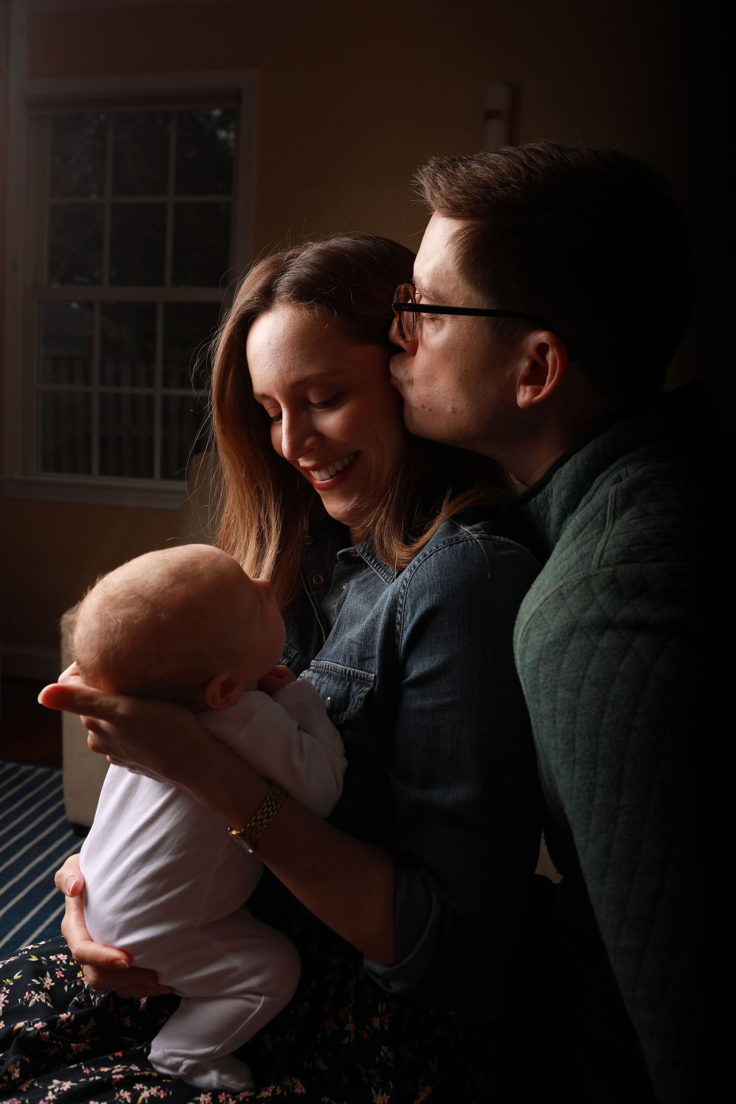 A couple sharing a tender moment with their newborn baby in a warmly lit room.