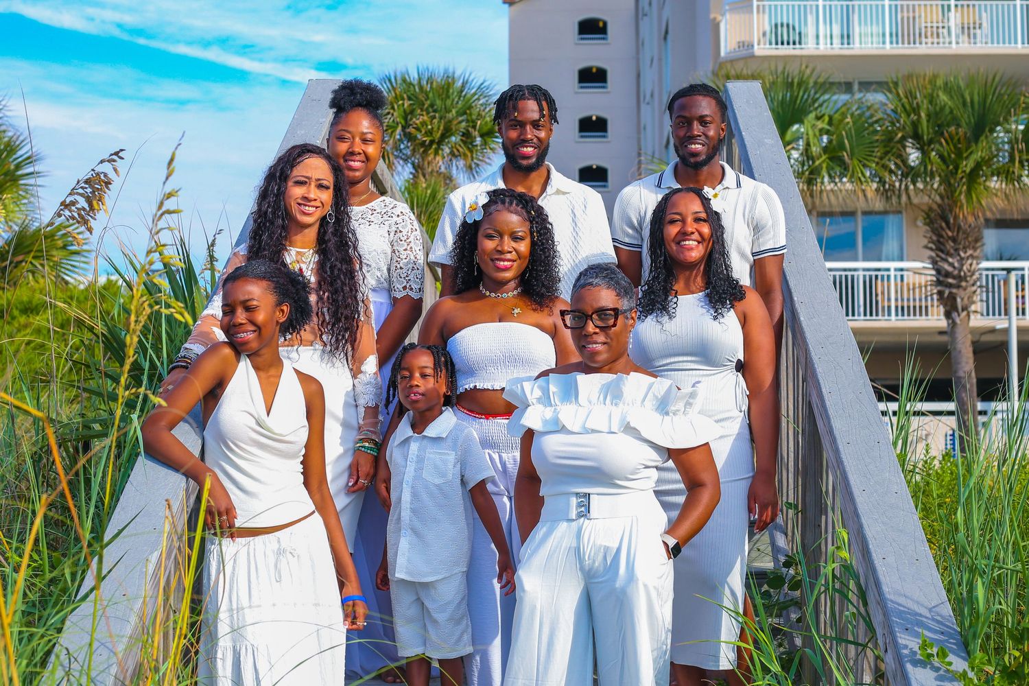 A family dressed in white poses for photos on a sunny beach with palm trees and condos in background.