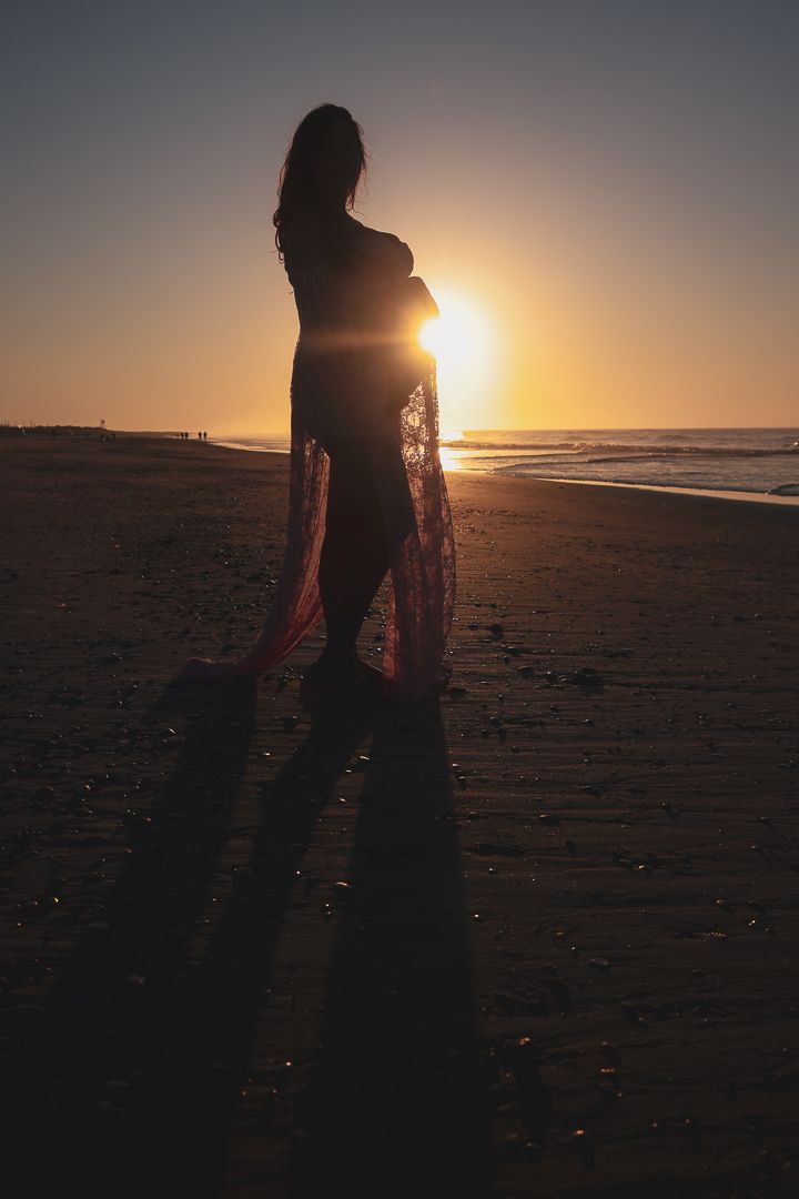 Silhouettes of people walking on beach at sunset creating dramatic shadows against golden sky.