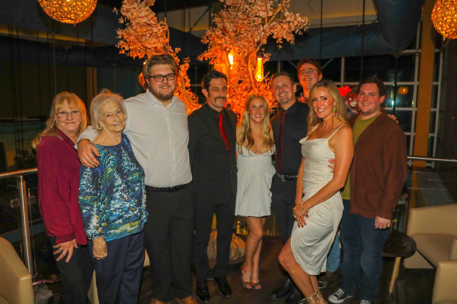 Group of nine people posing together indoors at an elegant evening event with warm decorative lighting.