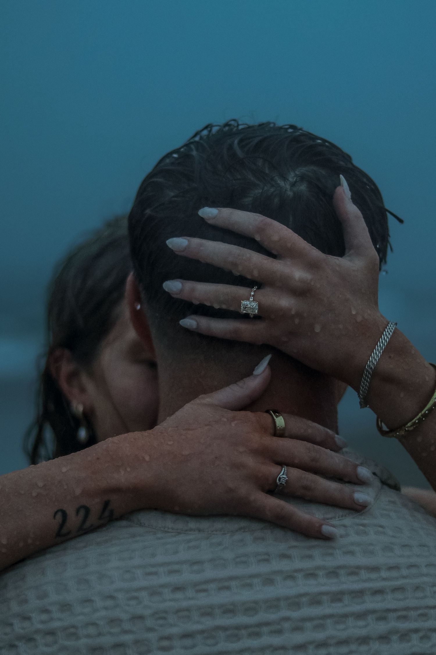 Couple embracing in rain, woman with diamond ring and bracelet holding man's head tenderly.