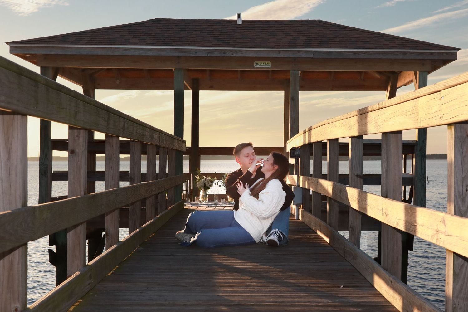 Couple sitting together on a wooden pier gazebo at golden hour by the water.
