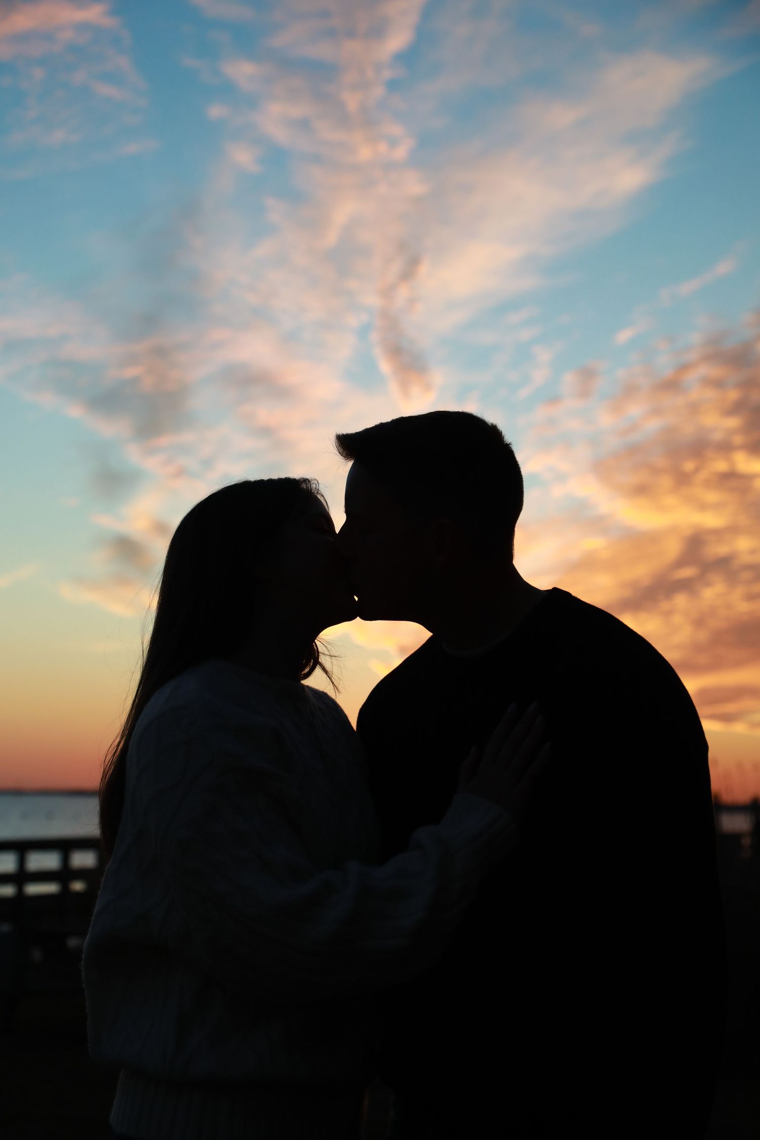 Silhouette of a couple kissing against a vibrant sunset sky with colorful clouds over the ocean.