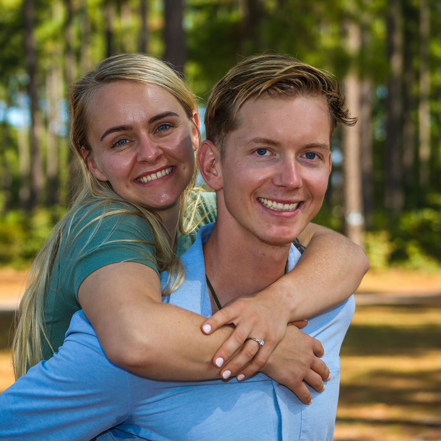 Happy couple sharing playful moments in a sunny forest setting wearing blue and teal.