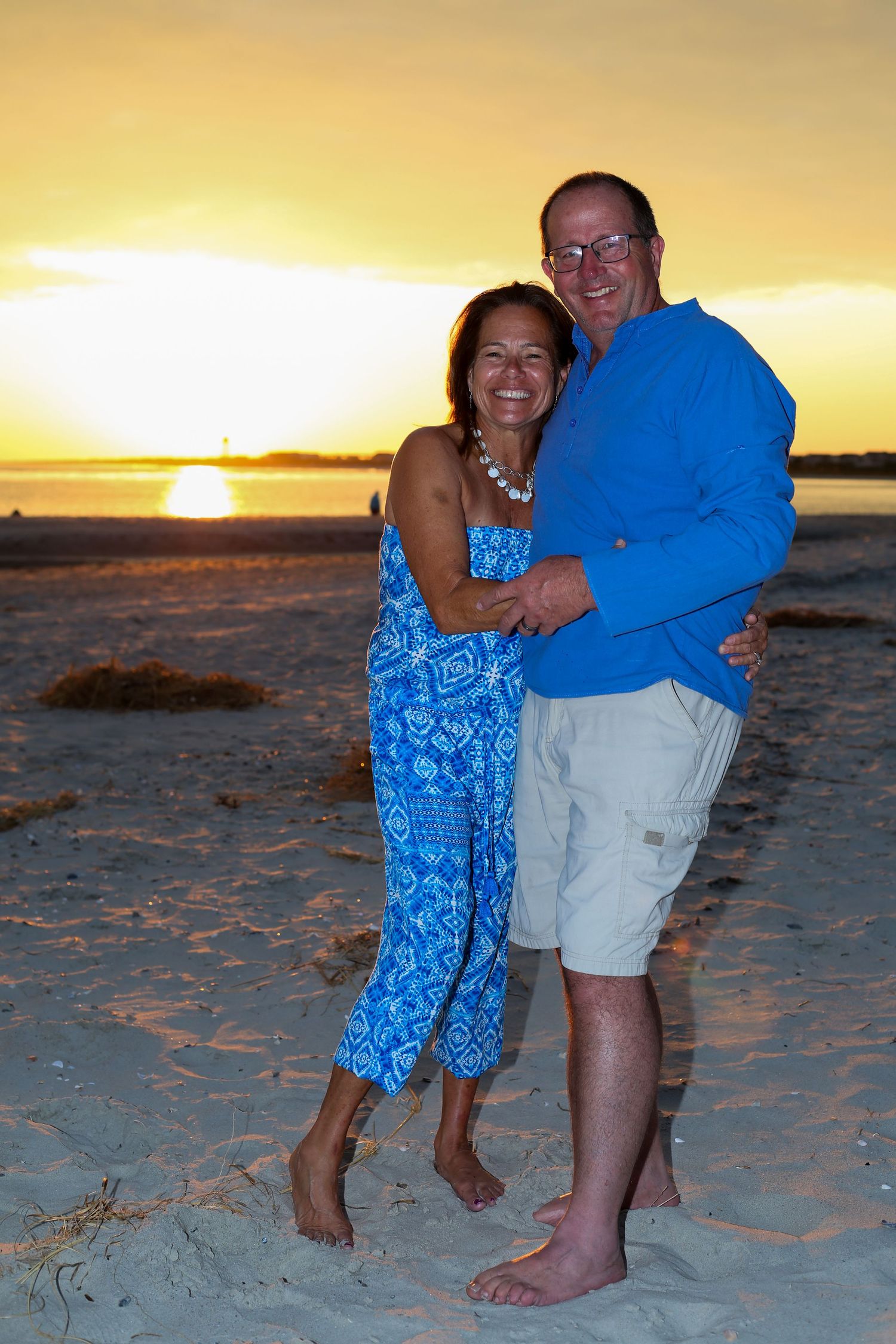 Couple embracing on beach at sunset with golden light.
