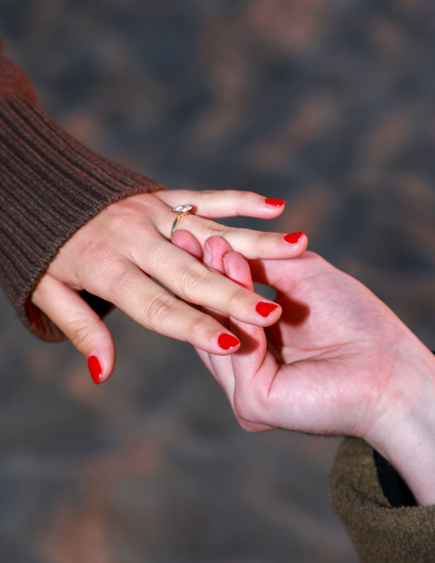 Close-up of two hands touching, woman wearing red nail polish and a gold engagement ring on her finger.