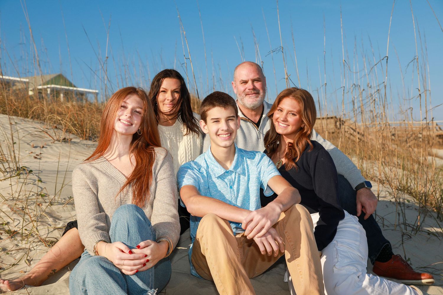Family of five smiling together on a sandy beach dune on a sunny day.