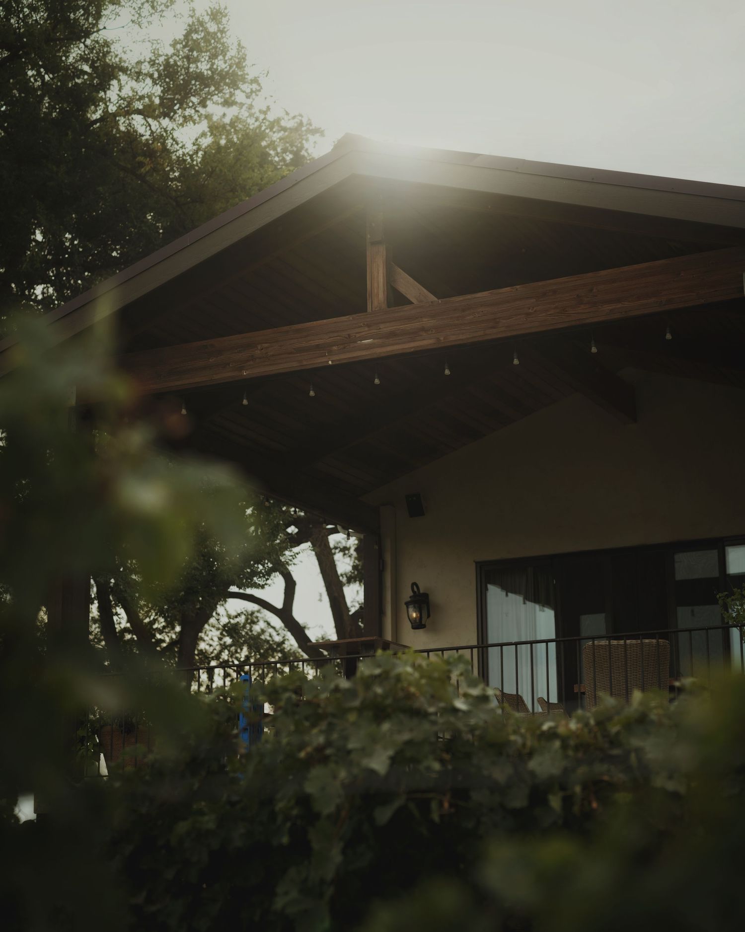A rustic wooden-beamed home exterior glows with golden sunlight filtering through lush green foliage at dusk.