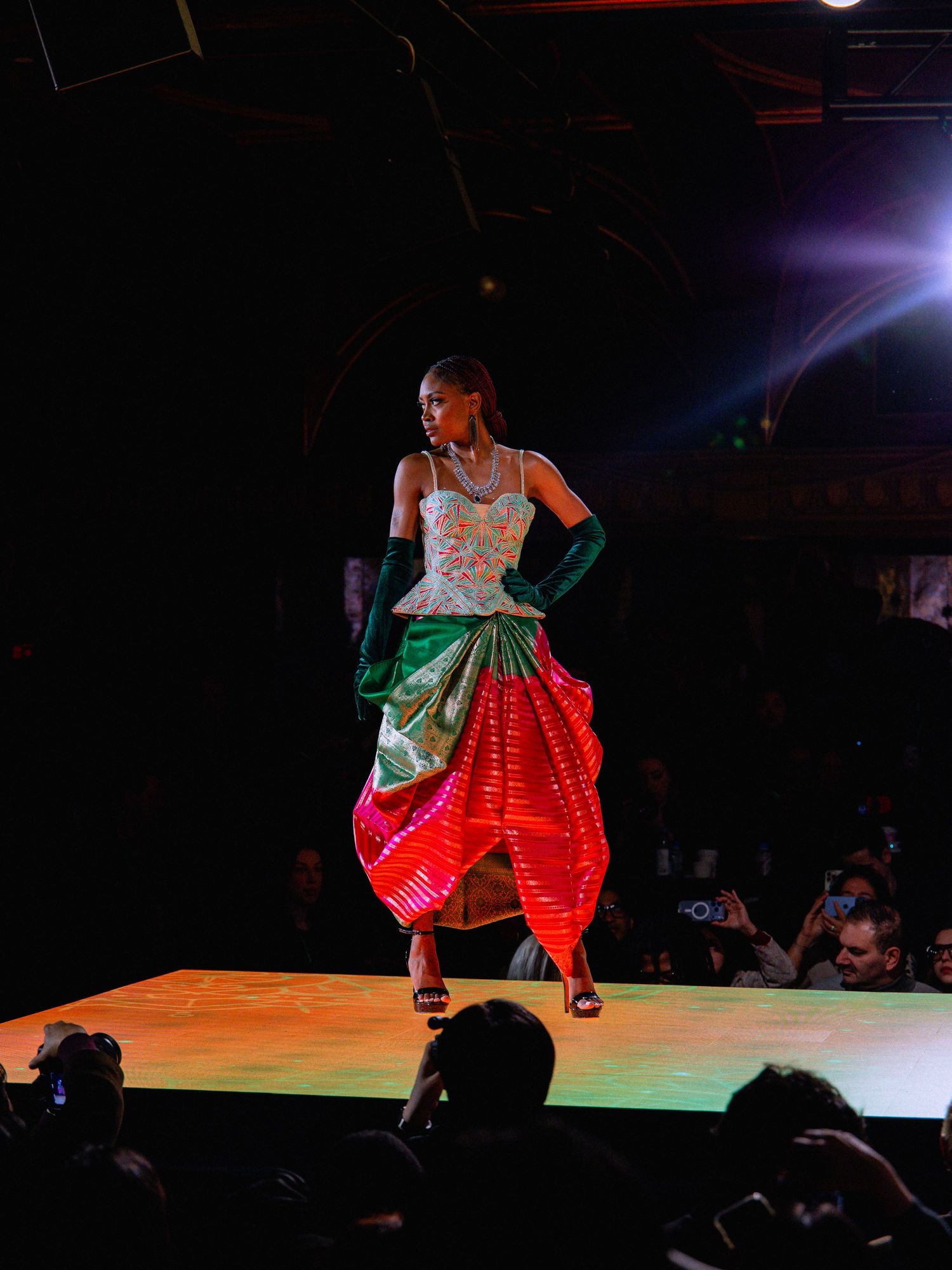 Performer in colorful LED light-up dress dances across dark stage during theatrical show.