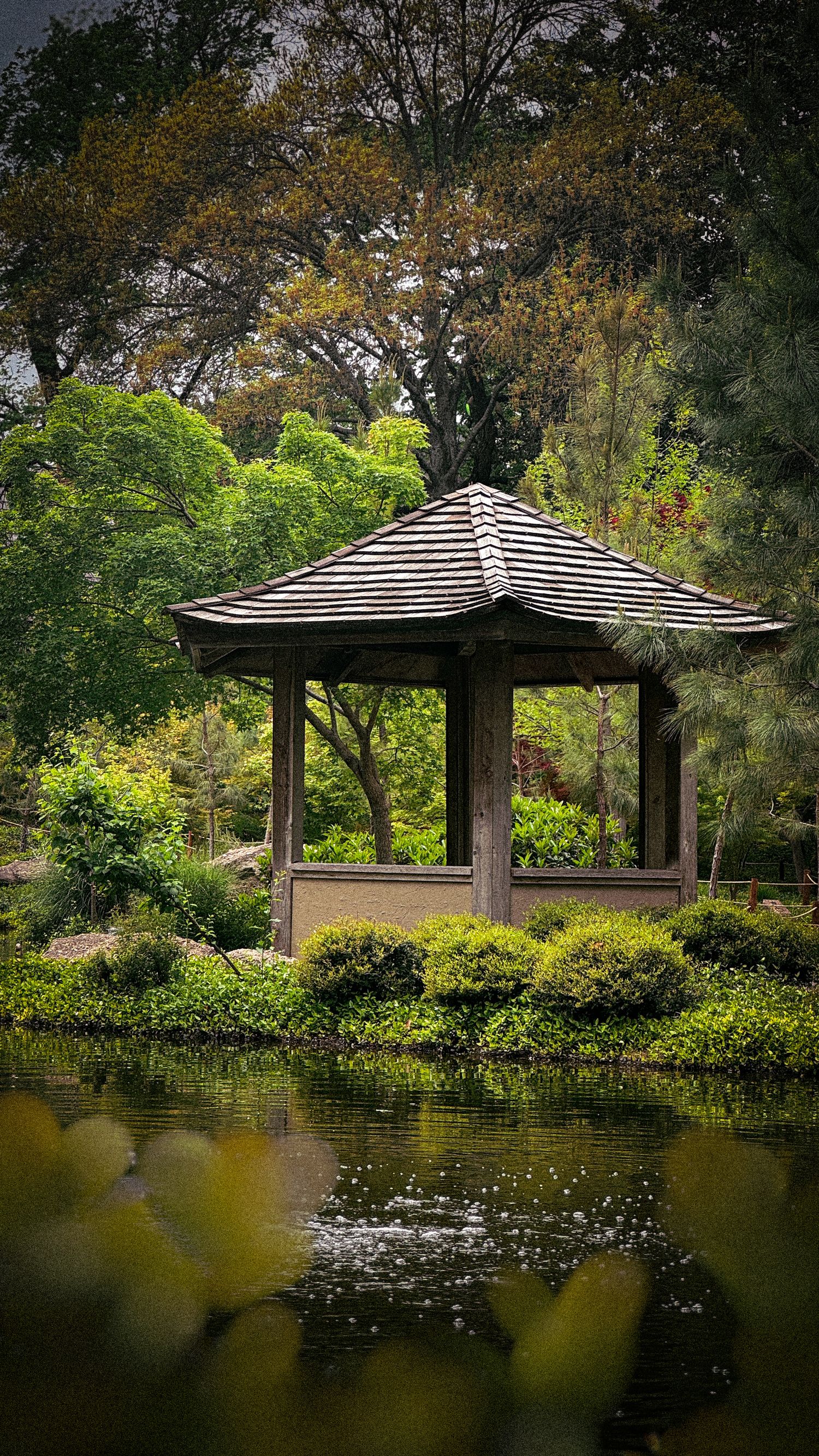 Japanese-style wooden gazebos overlooking a peaceful pond surrounded by lush greenery.