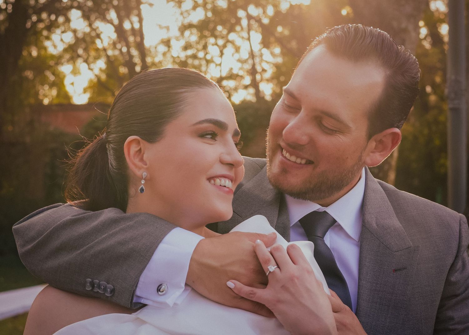 A romantic wedding couple embraces during golden hour sunset in an outdoor setting.