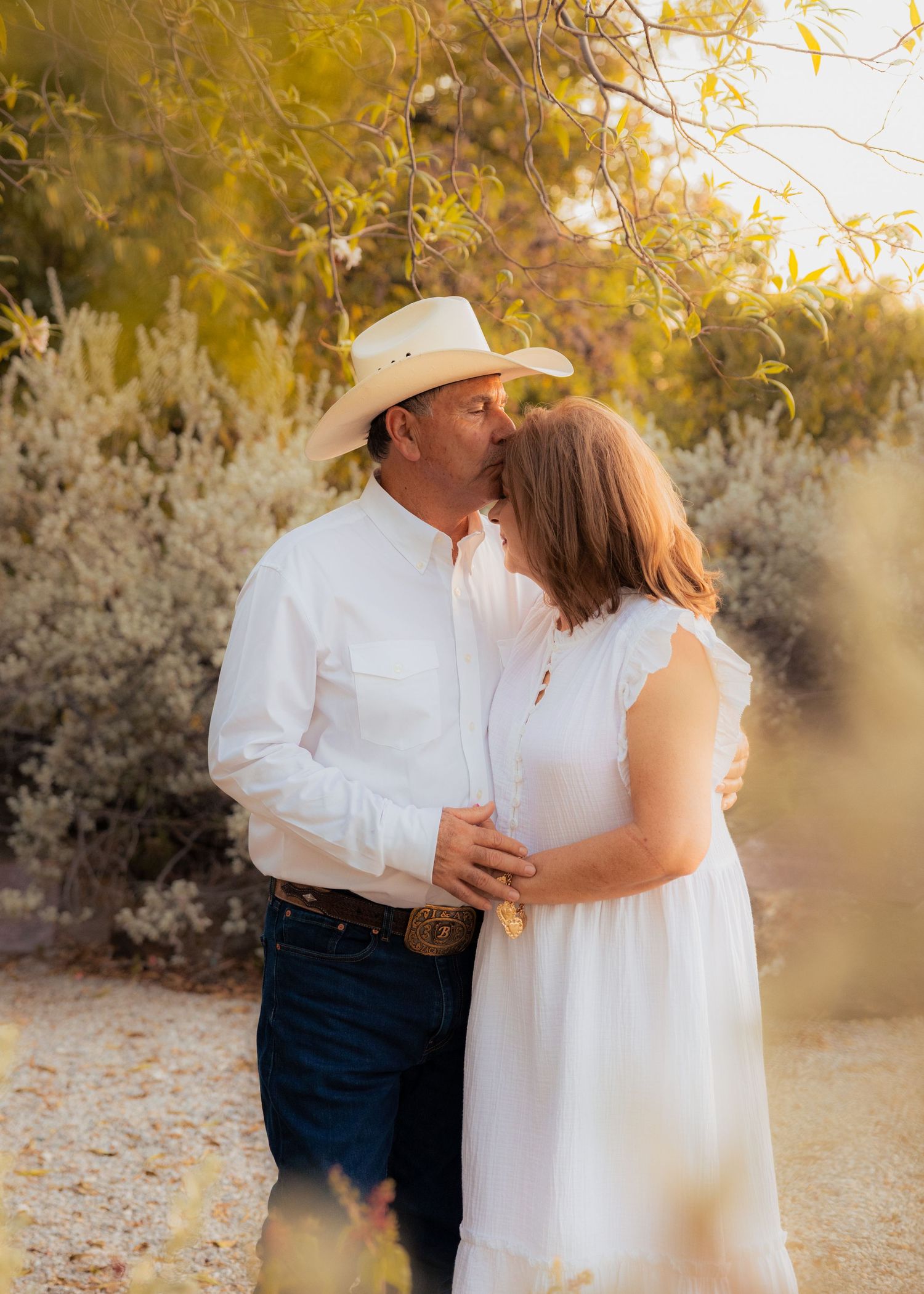Couple in white outfits embracing during sunset photoshoot in desert landscape.