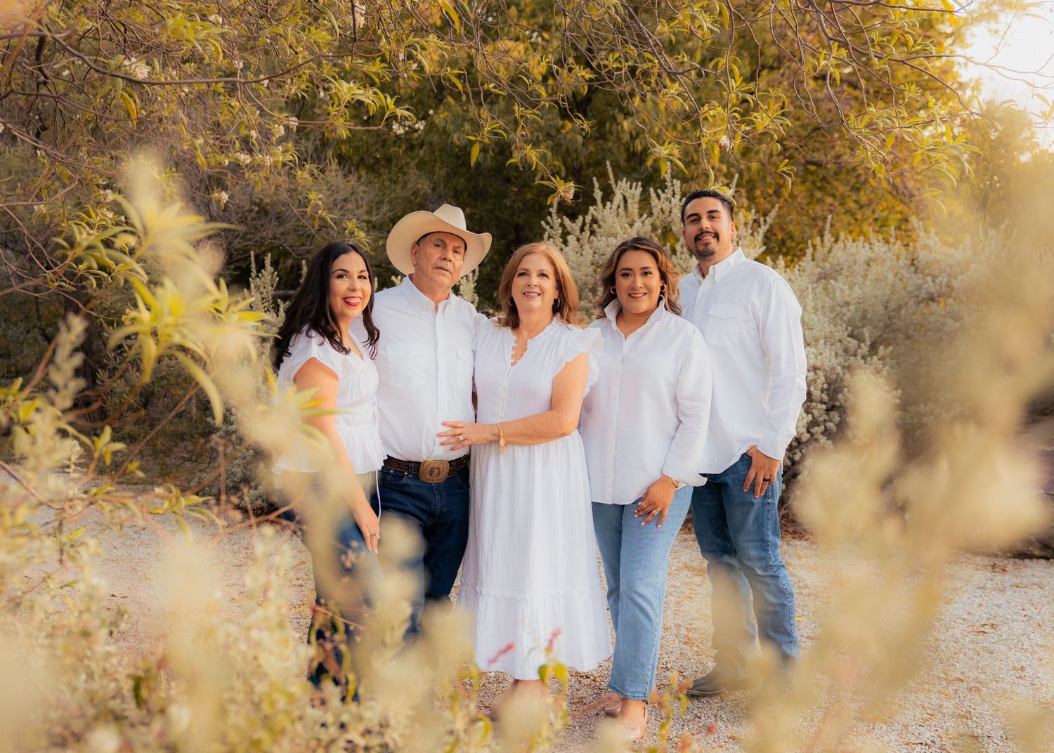 Family group poses together outdoors during golden hour with autumn foliage in background.