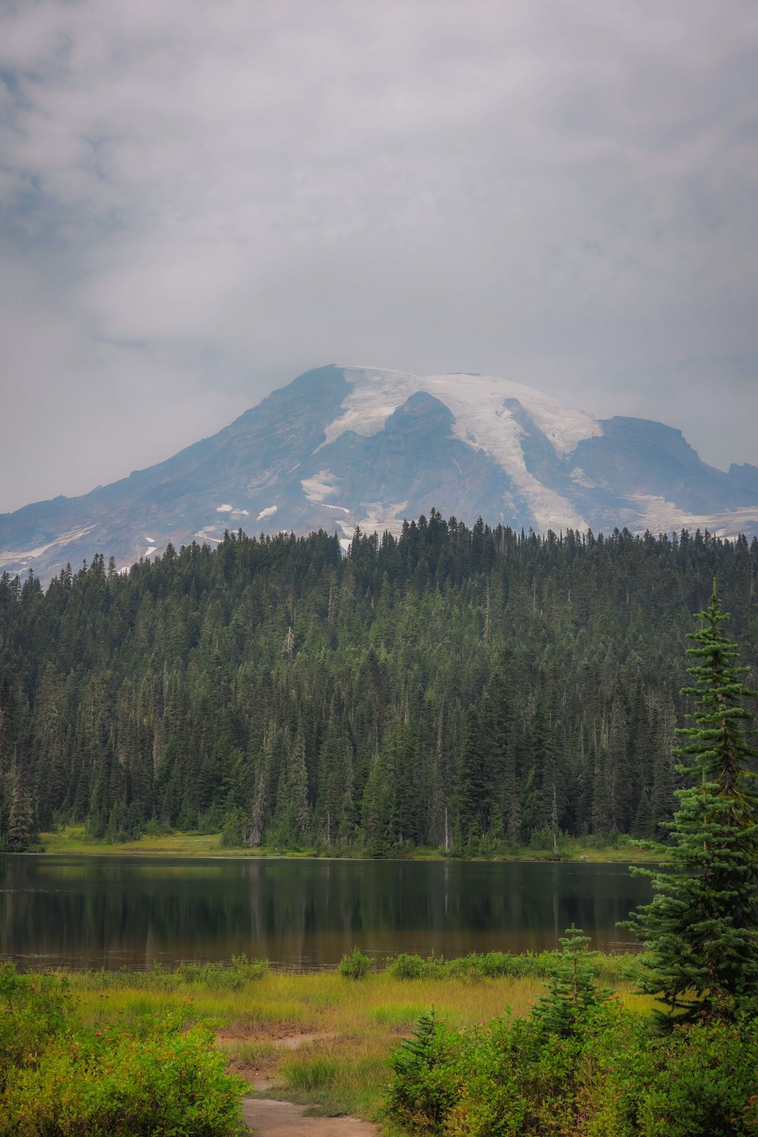 Mount Rainier rises majestically above evergreen forests and a serene alpine lake.