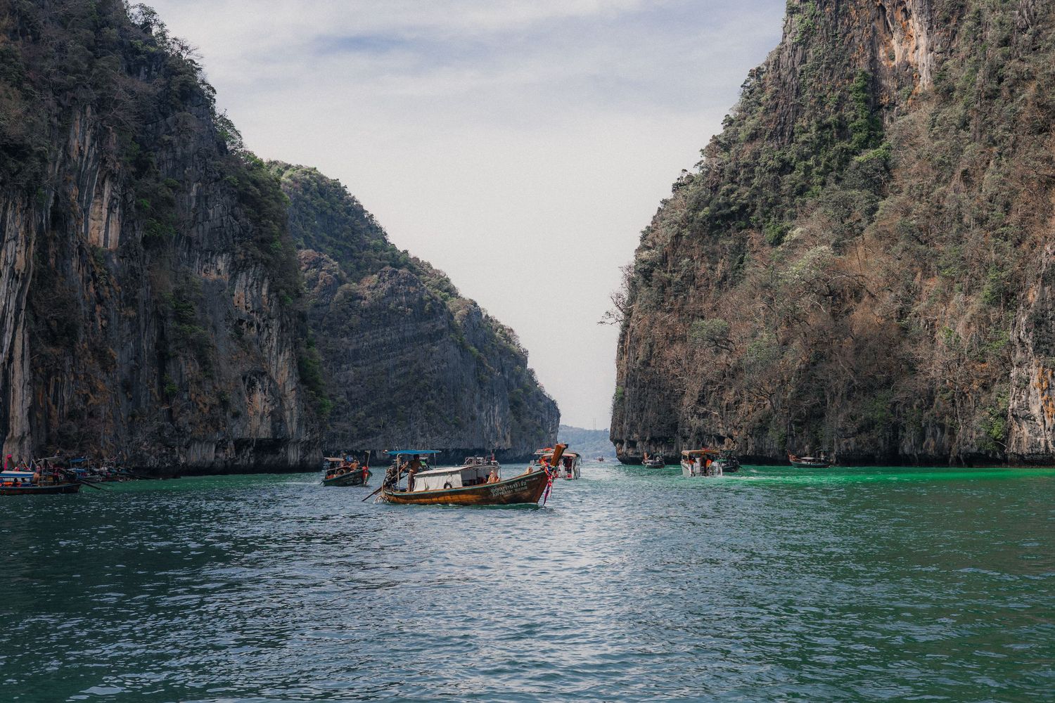 Longtail boats navigating turquoise waters between towering limestone cliffs in Phi Phi Islands, Thailand.