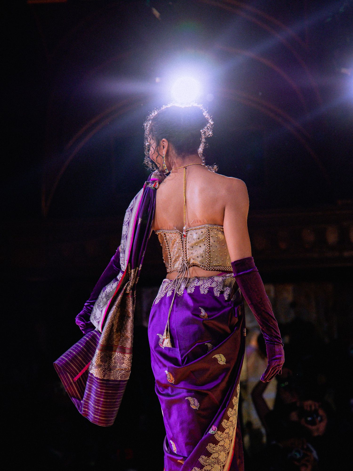 A performer in a shimmering purple dress dances on stage under dramatic lighting during a theatrical show.