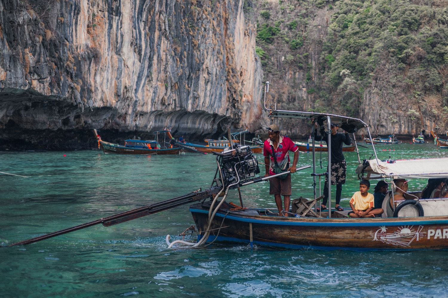 Longtail boats near dramatic limestone cliffs in turquoise waters of Phi Phi Islands, Thailand, with fishermen working on deck.