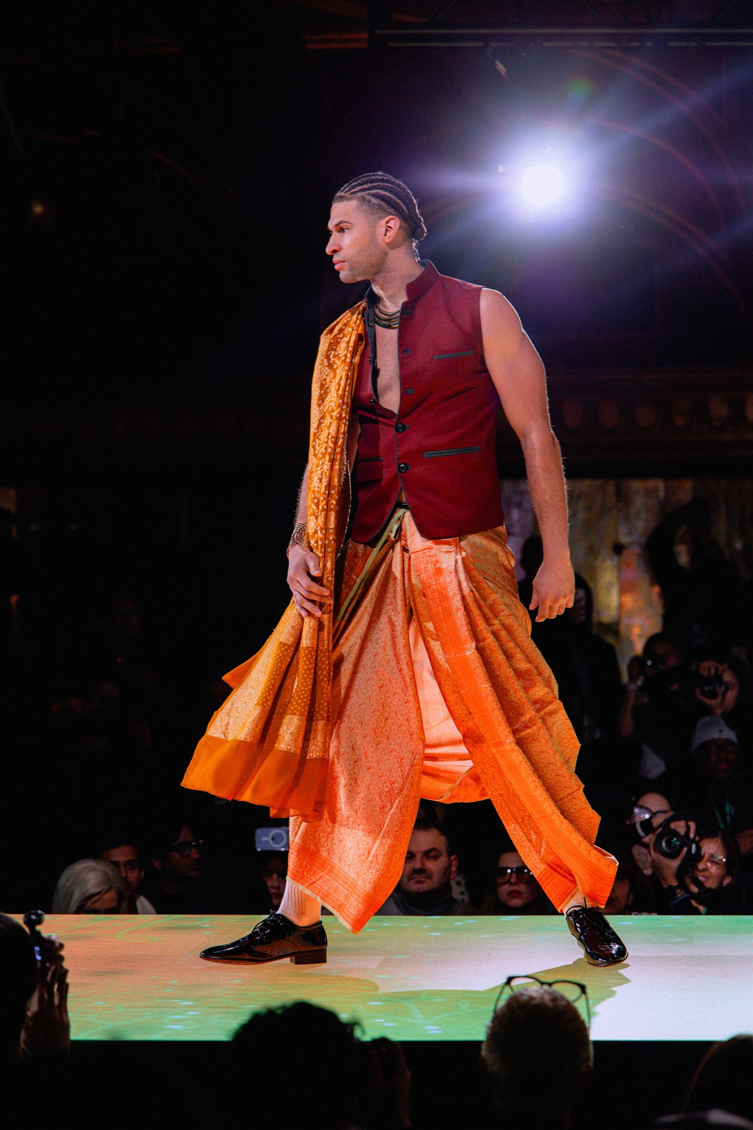 Dancer in red top and flowing orange skirt performs dynamic movements on illuminated stage during performance.