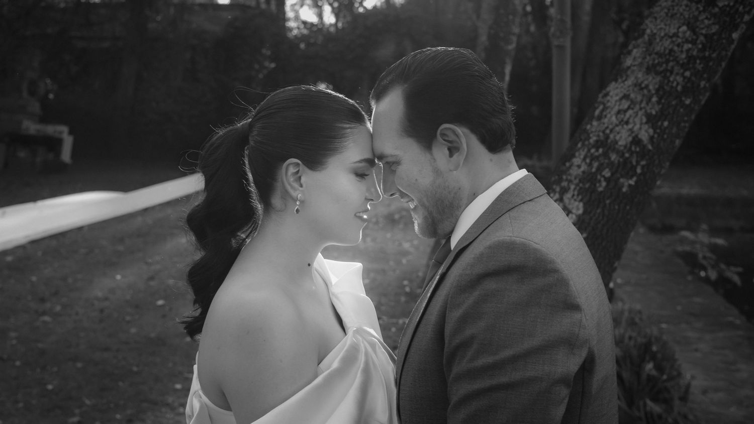 A black and white portrait of a couple sharing an intimate moment outdoors.