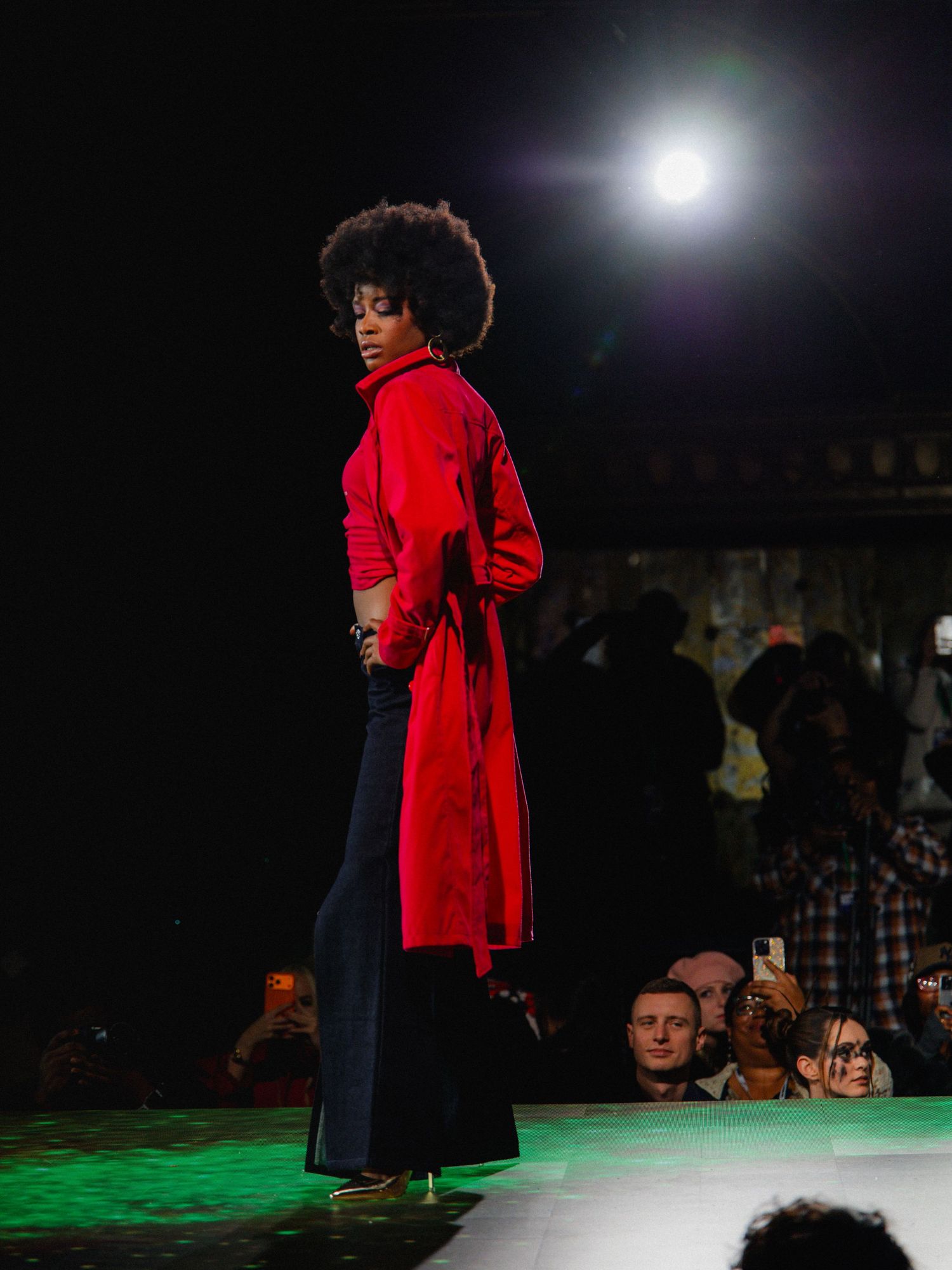 A performer in a red coat and dark pants dances expressively on a dimly lit stage with dramatic lighting effects.