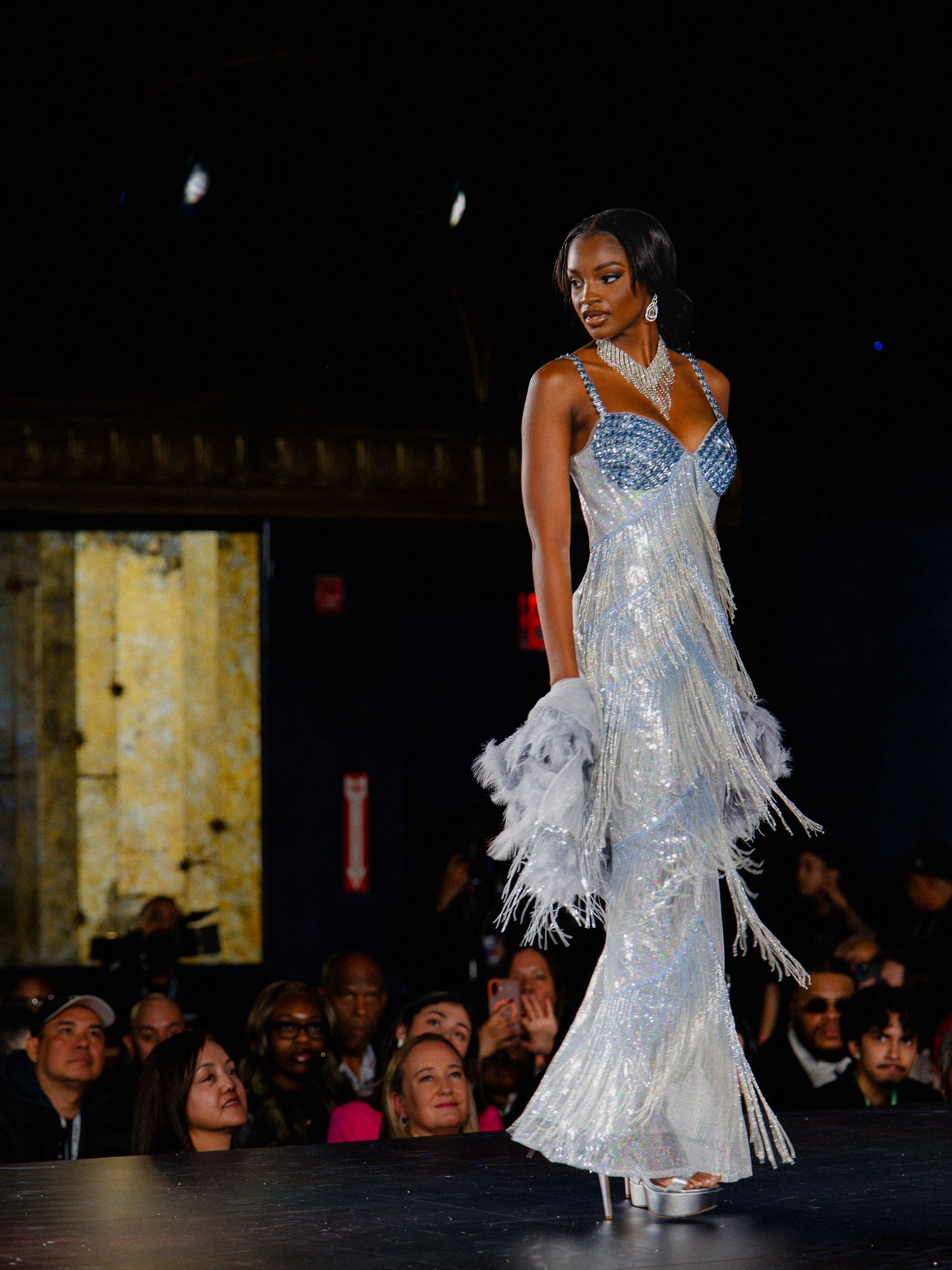 A model walks the runway in a shimmering white feathered dress with silver sequins during a fashion show.
