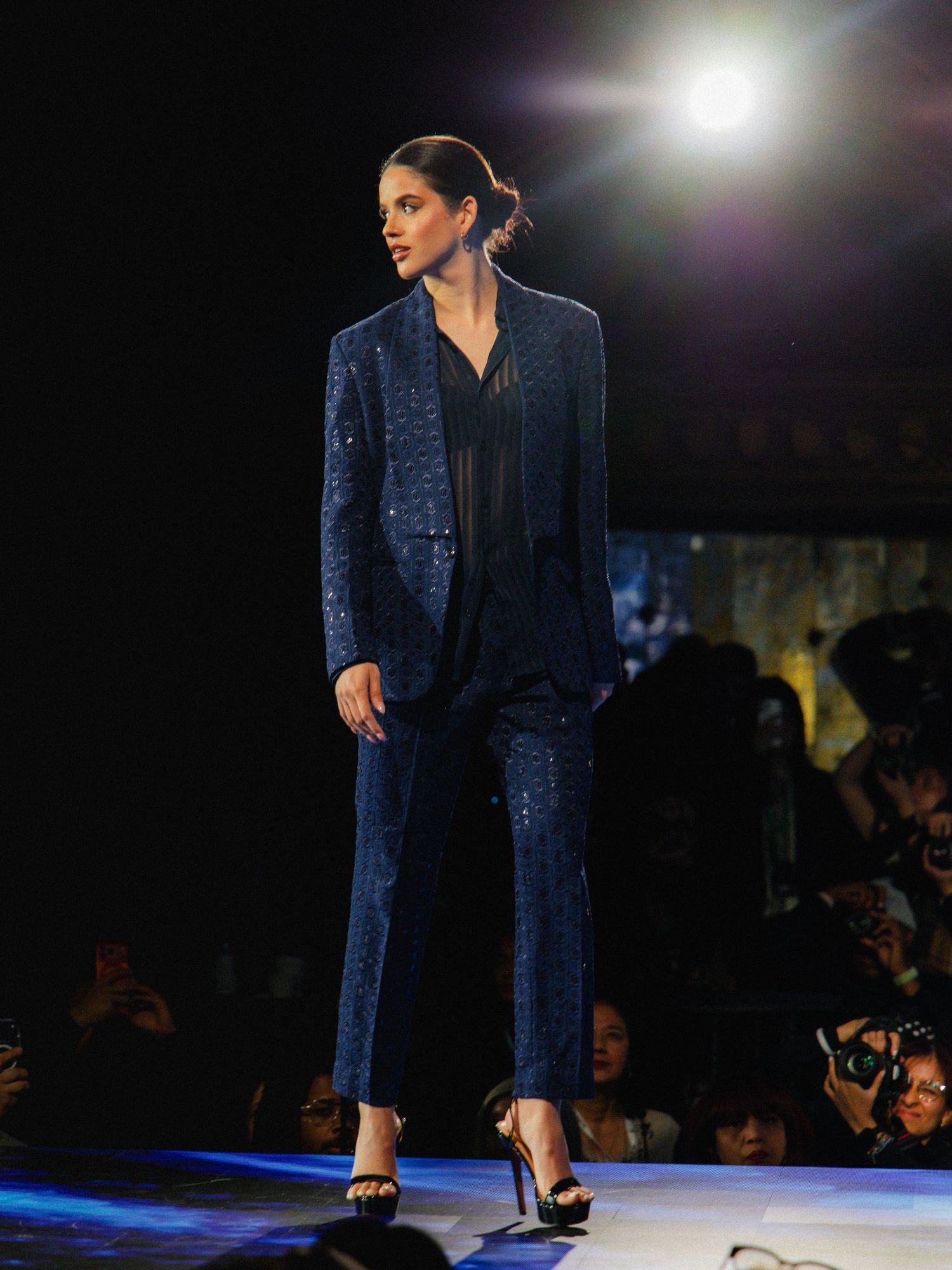 Model walks the runway in a dark blue velvet pantsuit and black heels during an evening fashion show.