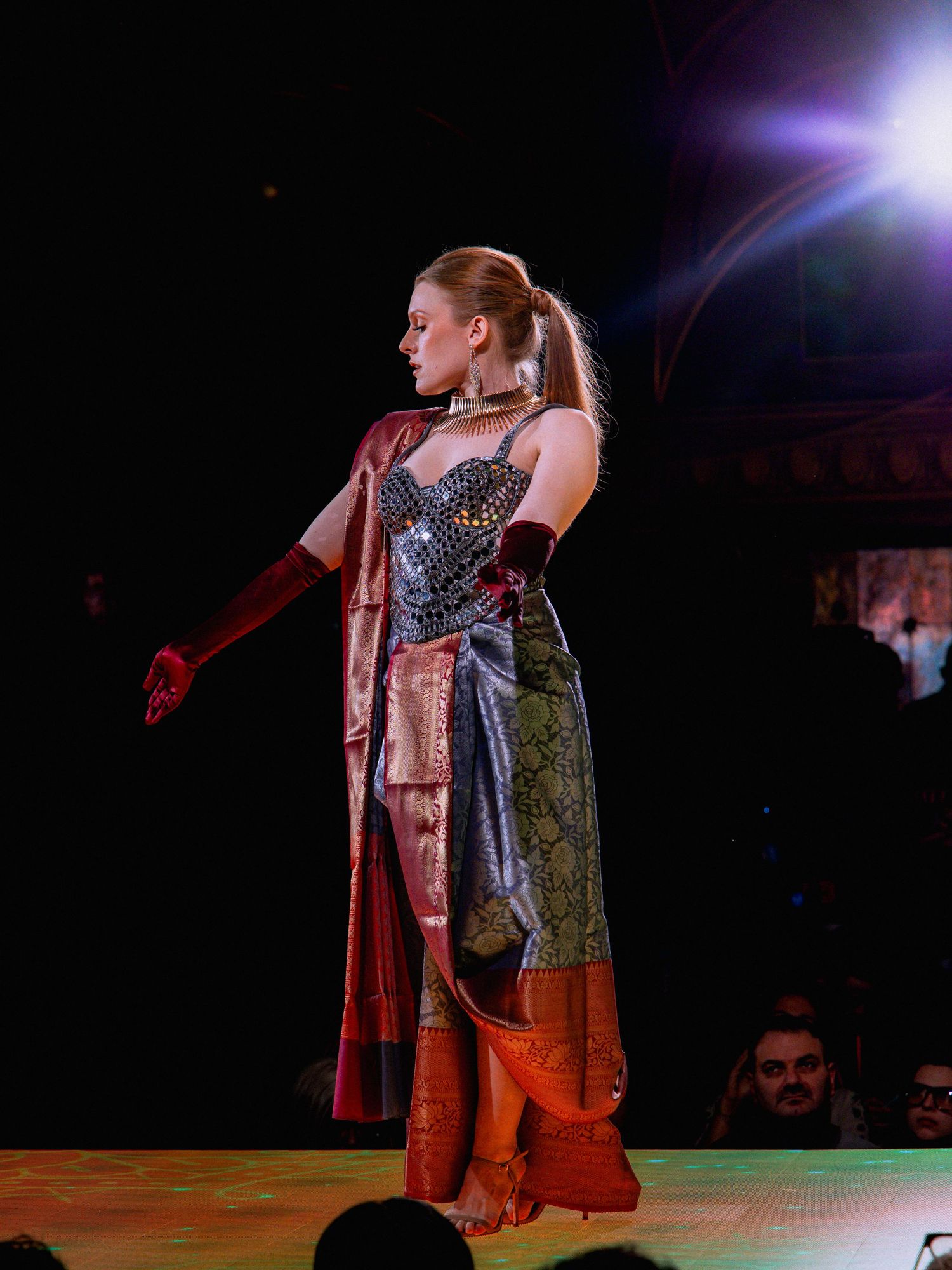 A performer in an orange skirt and dark top strikes dramatic poses during a stage performance under theatrical lighting.