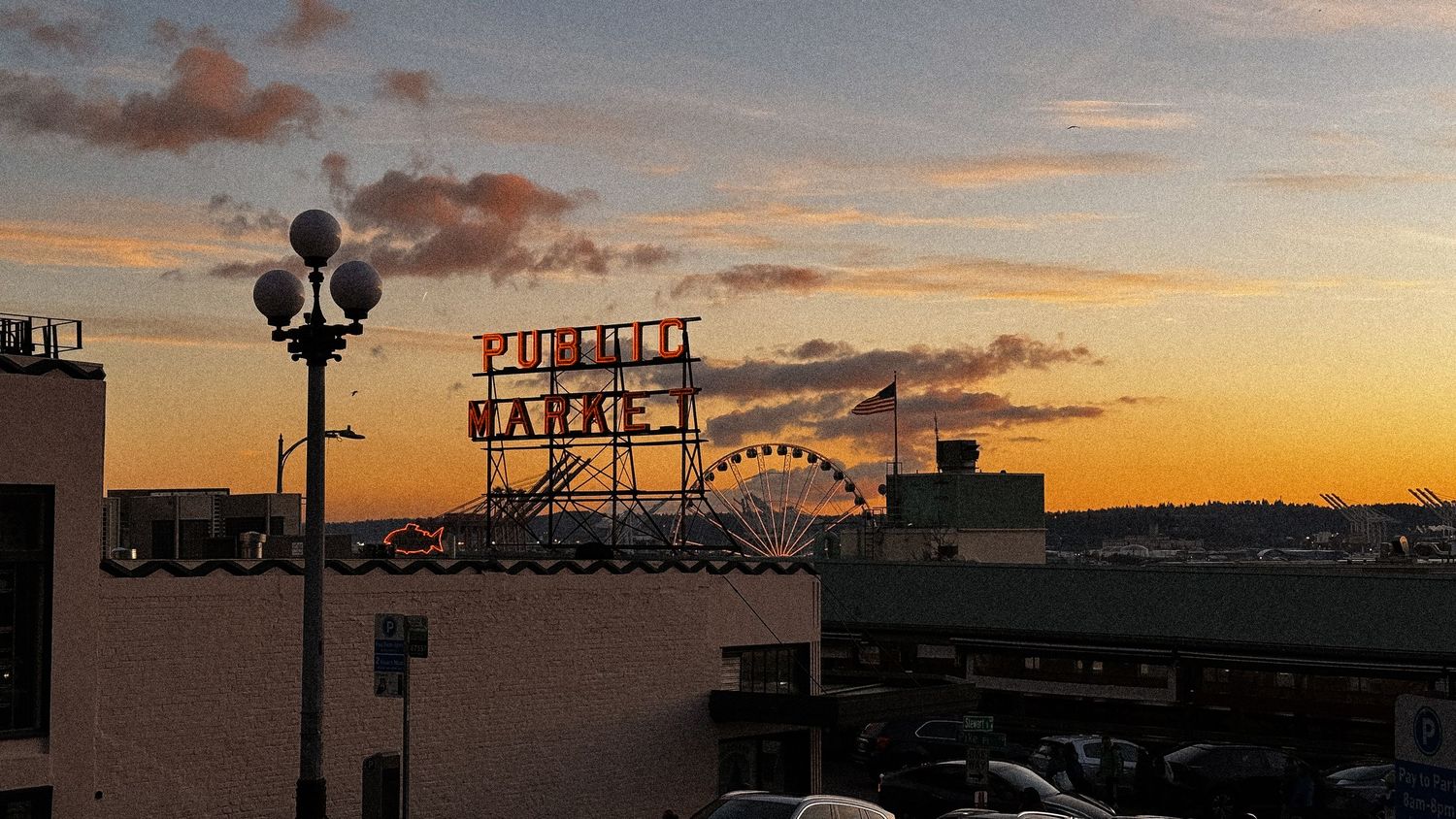 Silhouette of Seattle waterfront with Ferris wheel against orange sunset sky.